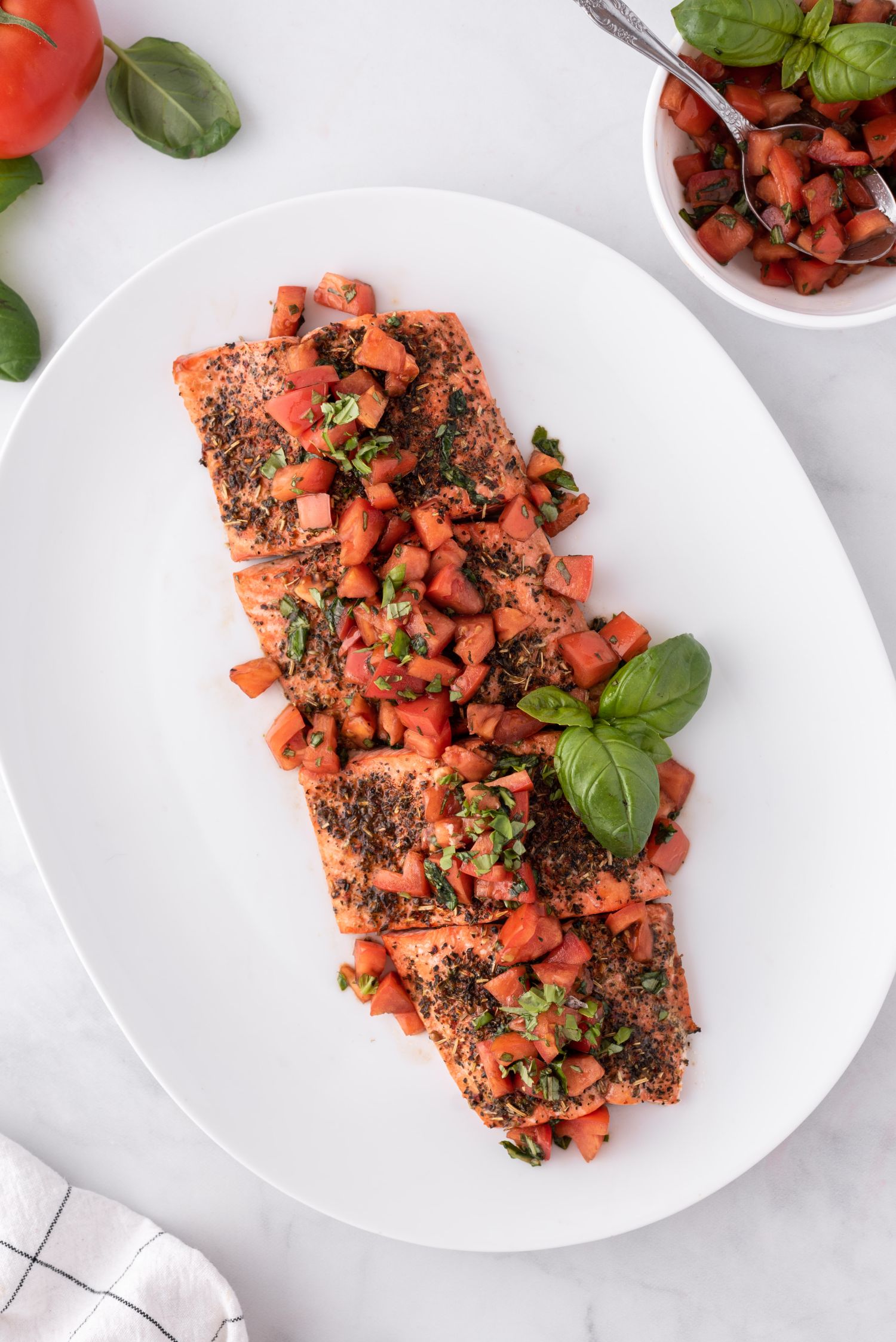 Baked Italian salmon with tomato basil salad on top on a large pate with fresh basil leaves.