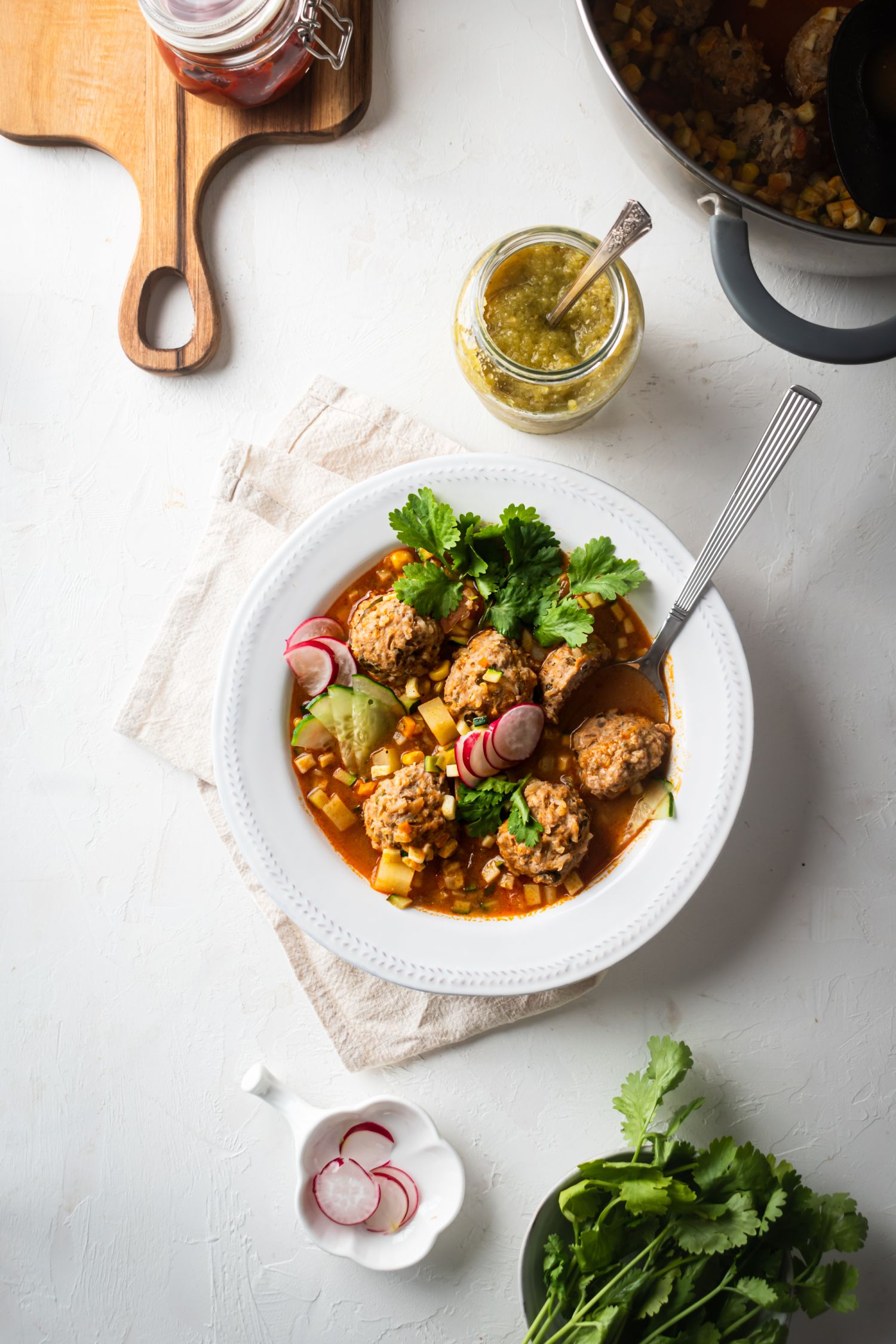 Mexican Albondigas soup with beef meatballs, vegetables, and potatoes served with fresh cilantro and radishes. 