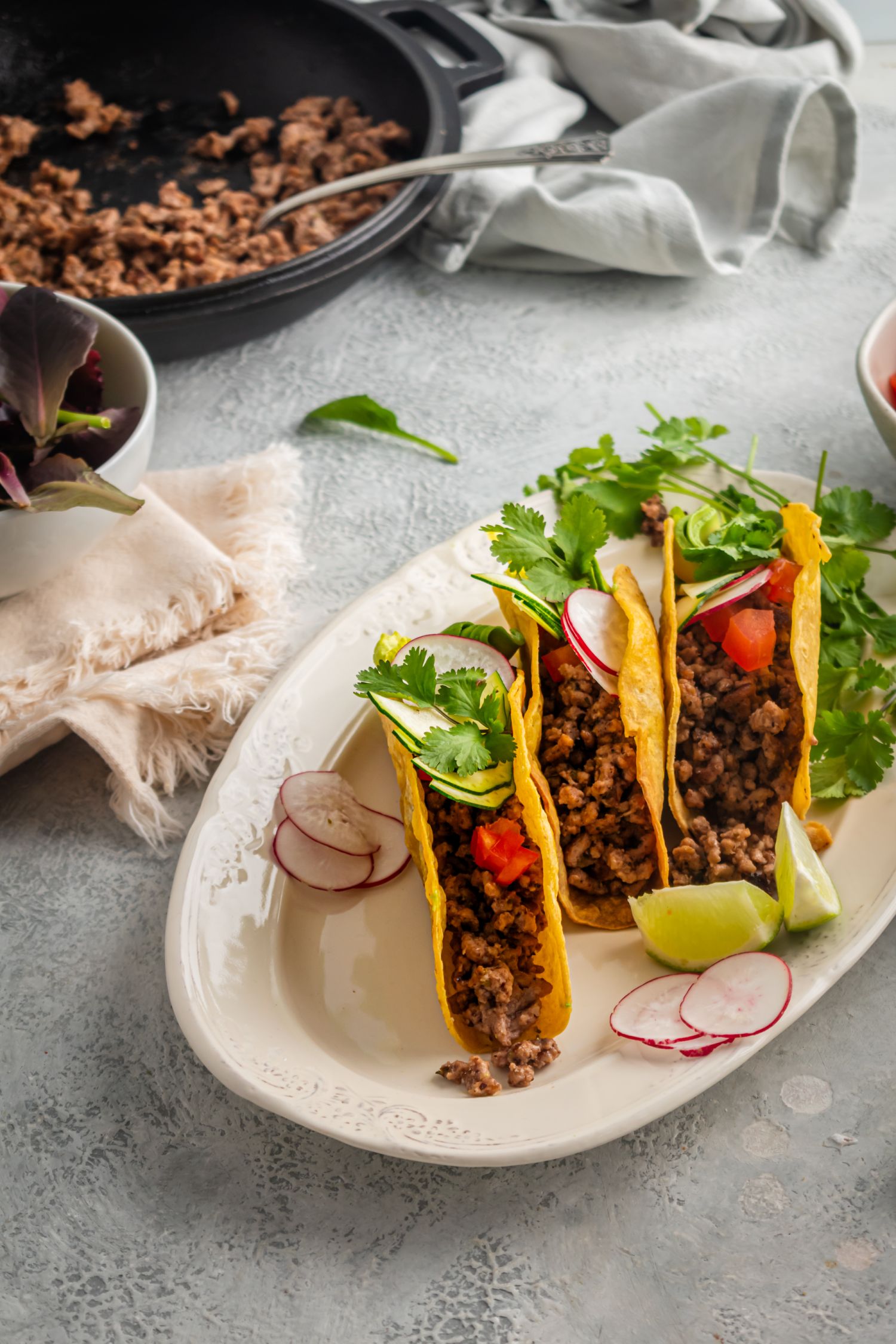 Crispy ground beef tacos with ancho chile powder served with lettuce, cilantro, tomatoes, and radishes.