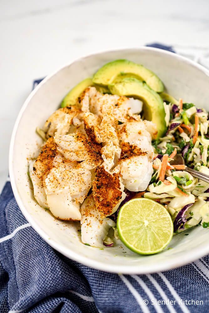 Fish taco bowl with seasoned cod served with coleslaw and sliced avocado.