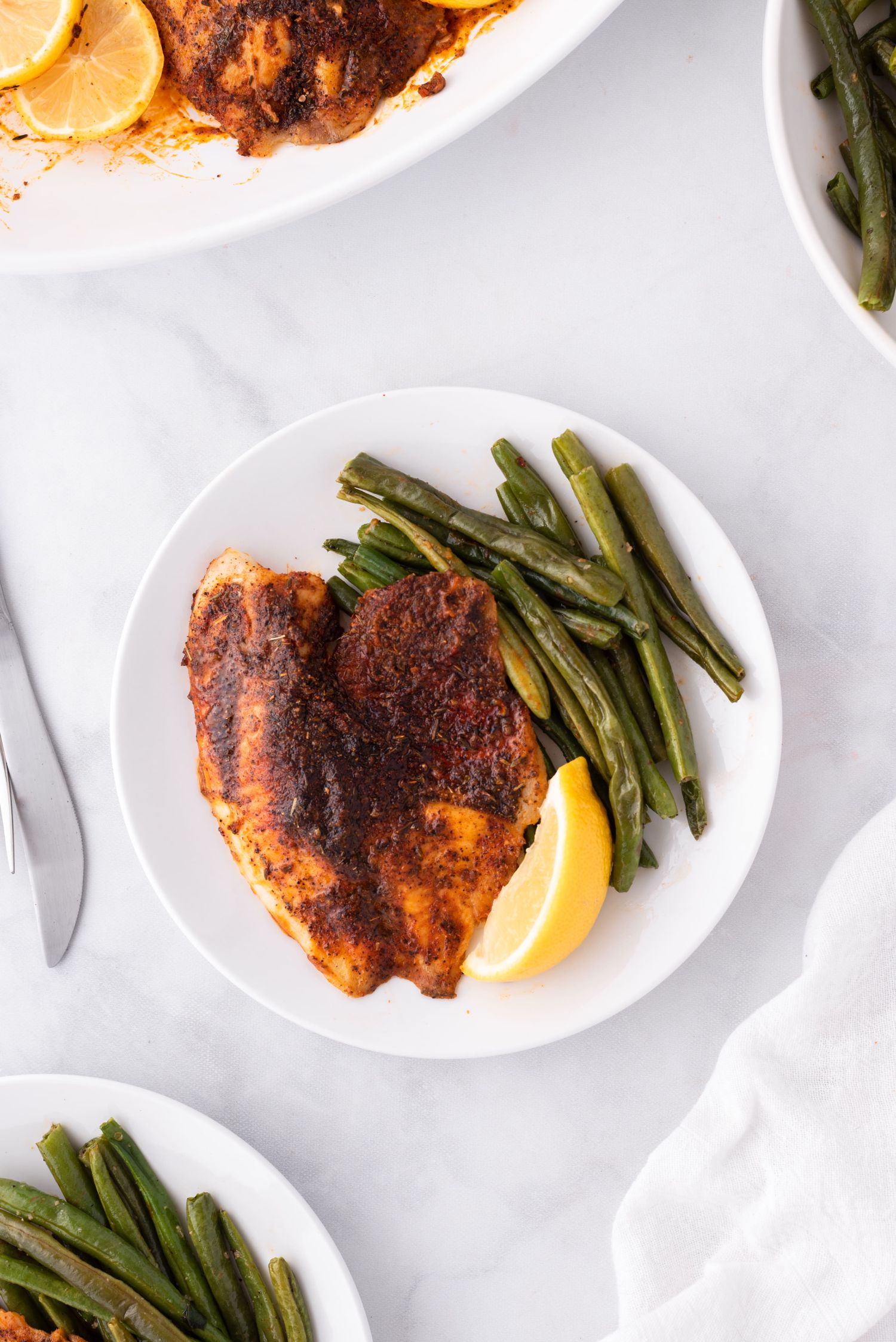 Tilapia with blackening seasoning on a plate with green beans and a lemon.