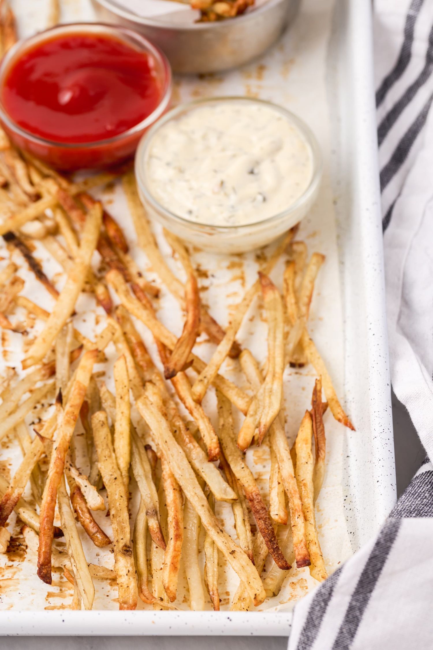 Crispy potato and turnip fries on a baking sheet served with small bowls of ranch and ketchup.