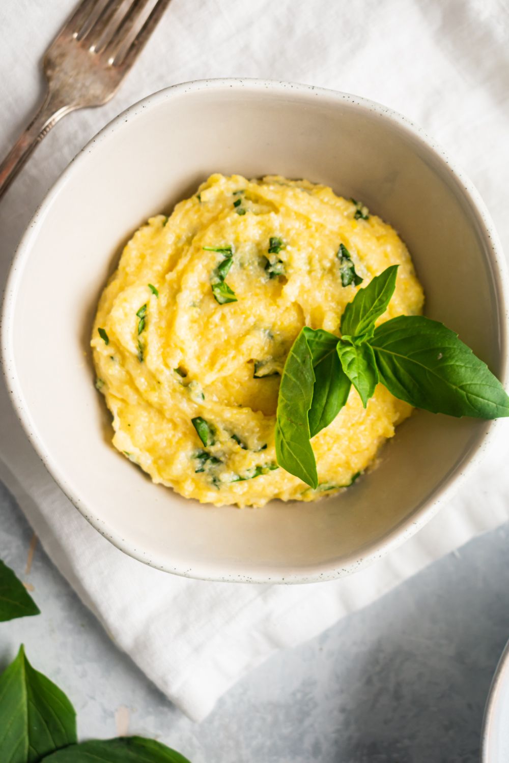 Creamy basil and parmesan polenta served in a white bowl with a white napkin.