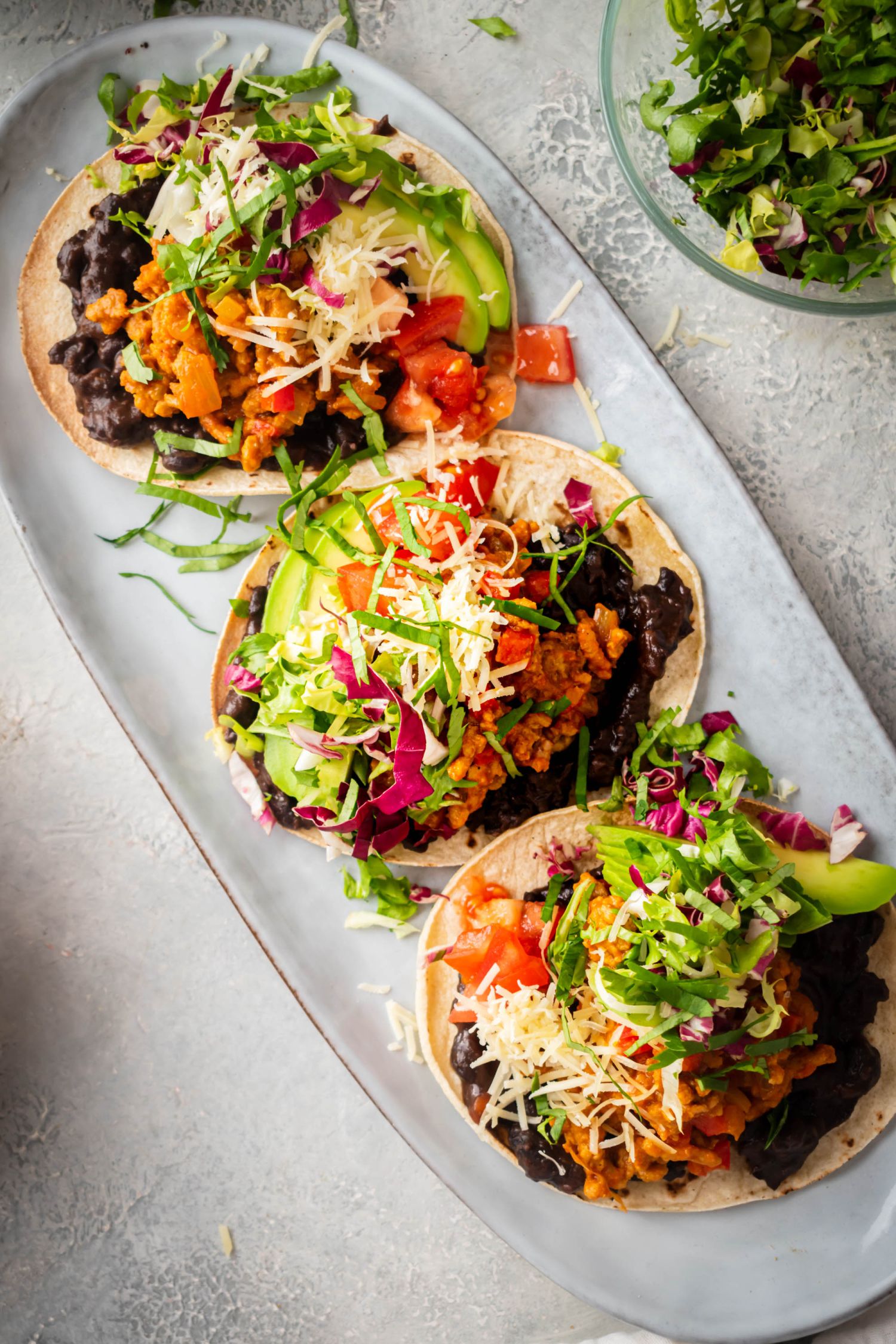 Homemade ground beef tostadas with corn tortillas topped with lettuce, tomato, cheese, and avocado.