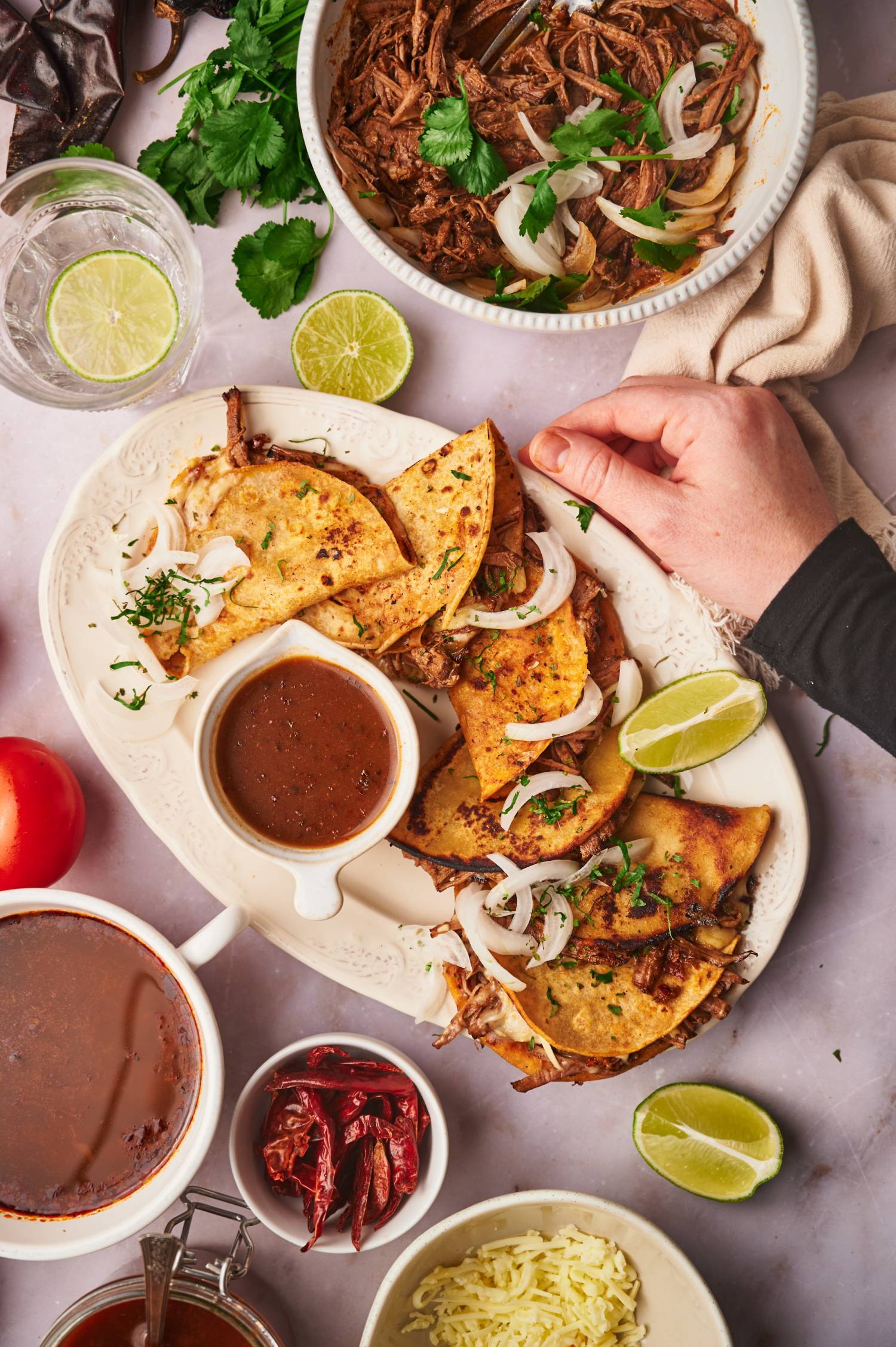 Fried birria tacos on a platter with consome, onions, lime, and extra birria on the side.