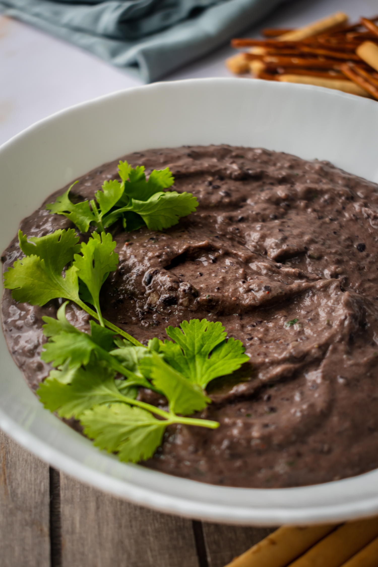 A bowl of black bean hummus with creamy black beans, olive oil, tahini, spices, and cilantro.