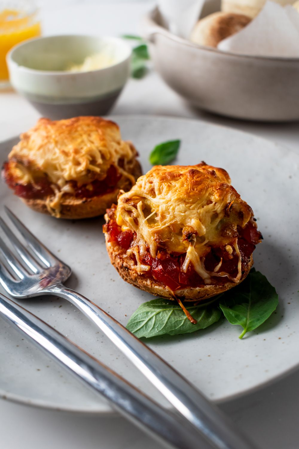 Scrambled egg breakfast pizzas on English muffins with melted mozzarella cheese and basil.