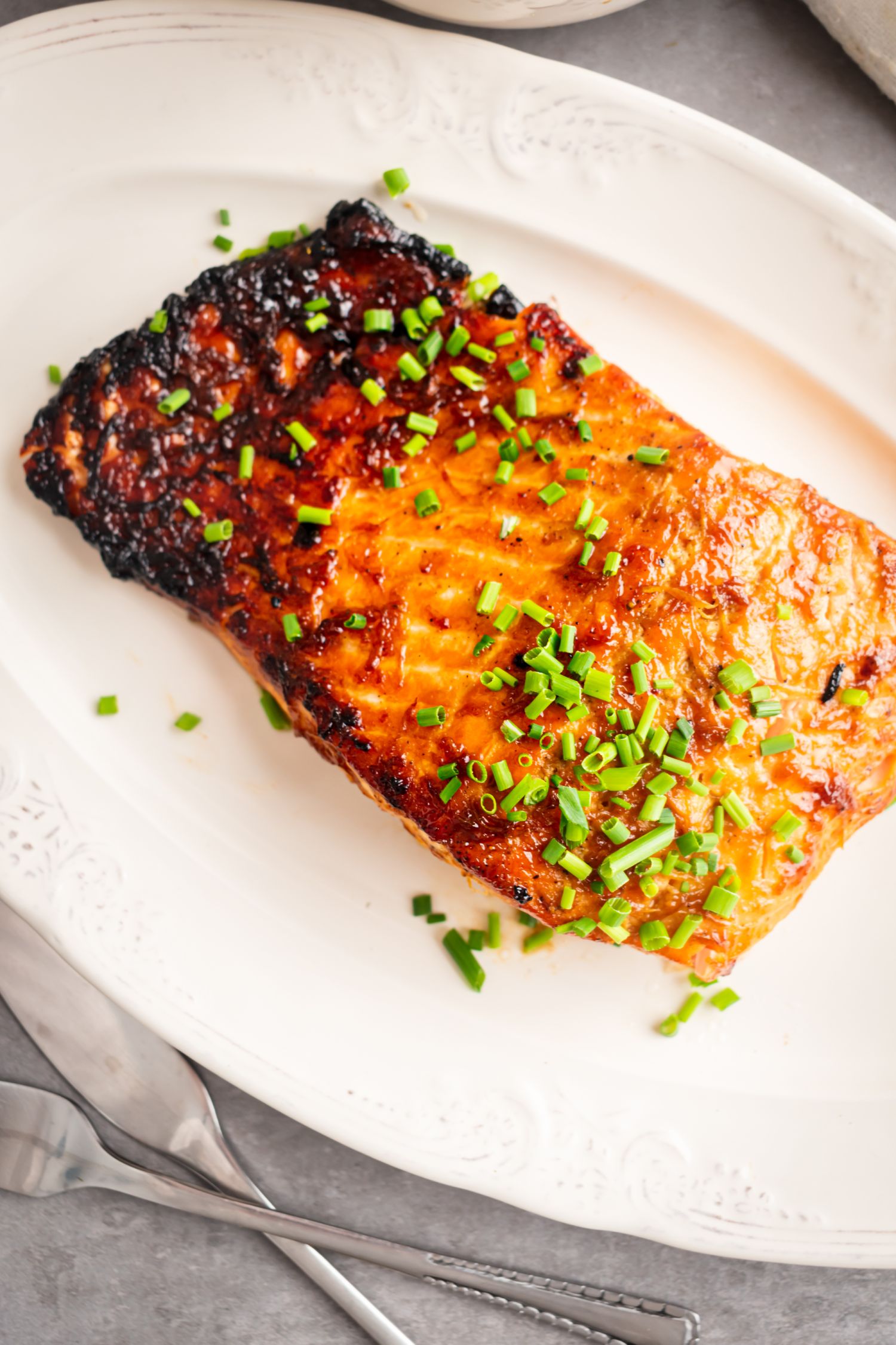 Glazed brown sugar salmon with crispy edges on a white plate with green onions.