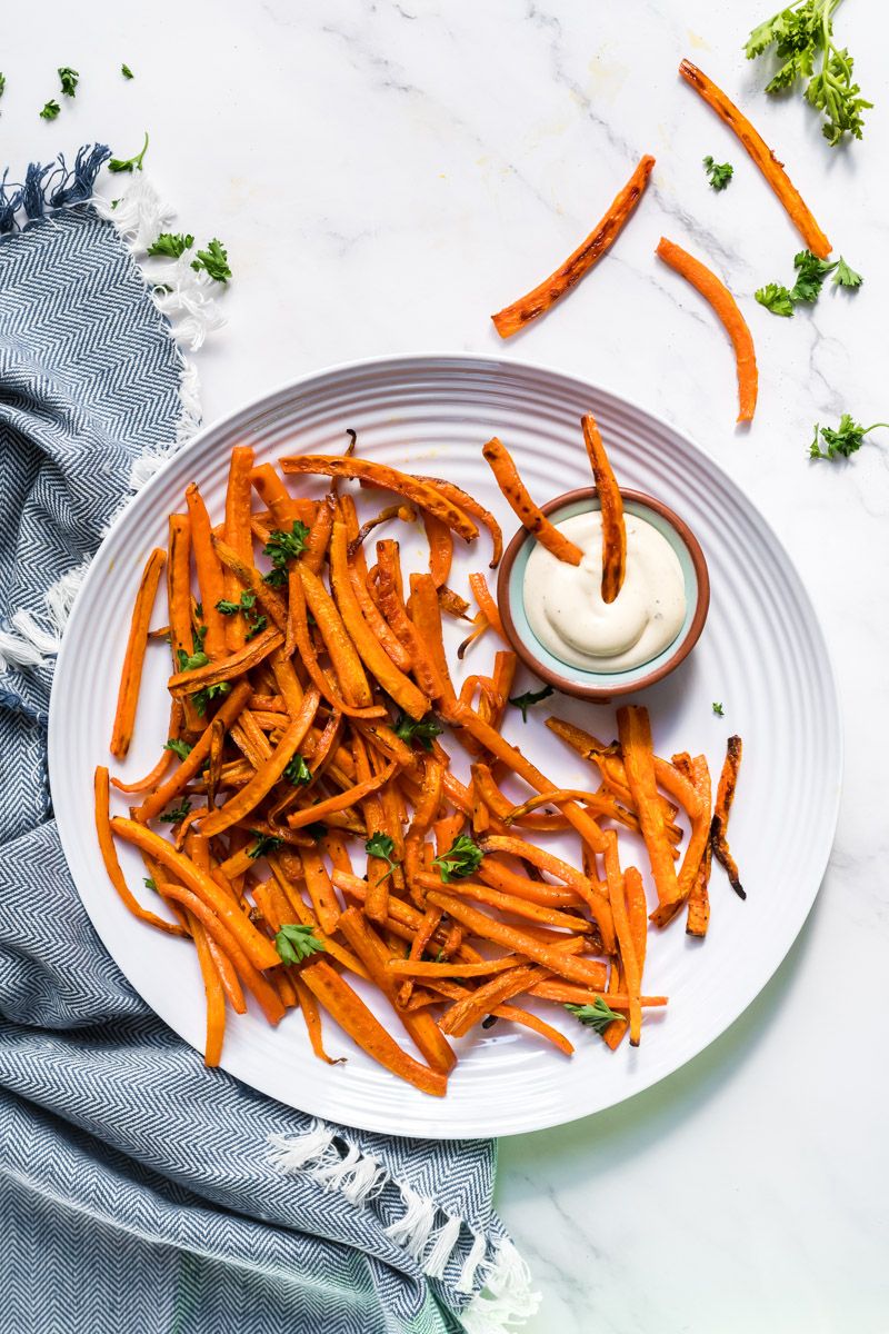 Crispy baked carrot fries served with fresh herbs, salt, and pepper on a plate with dipping sauce.