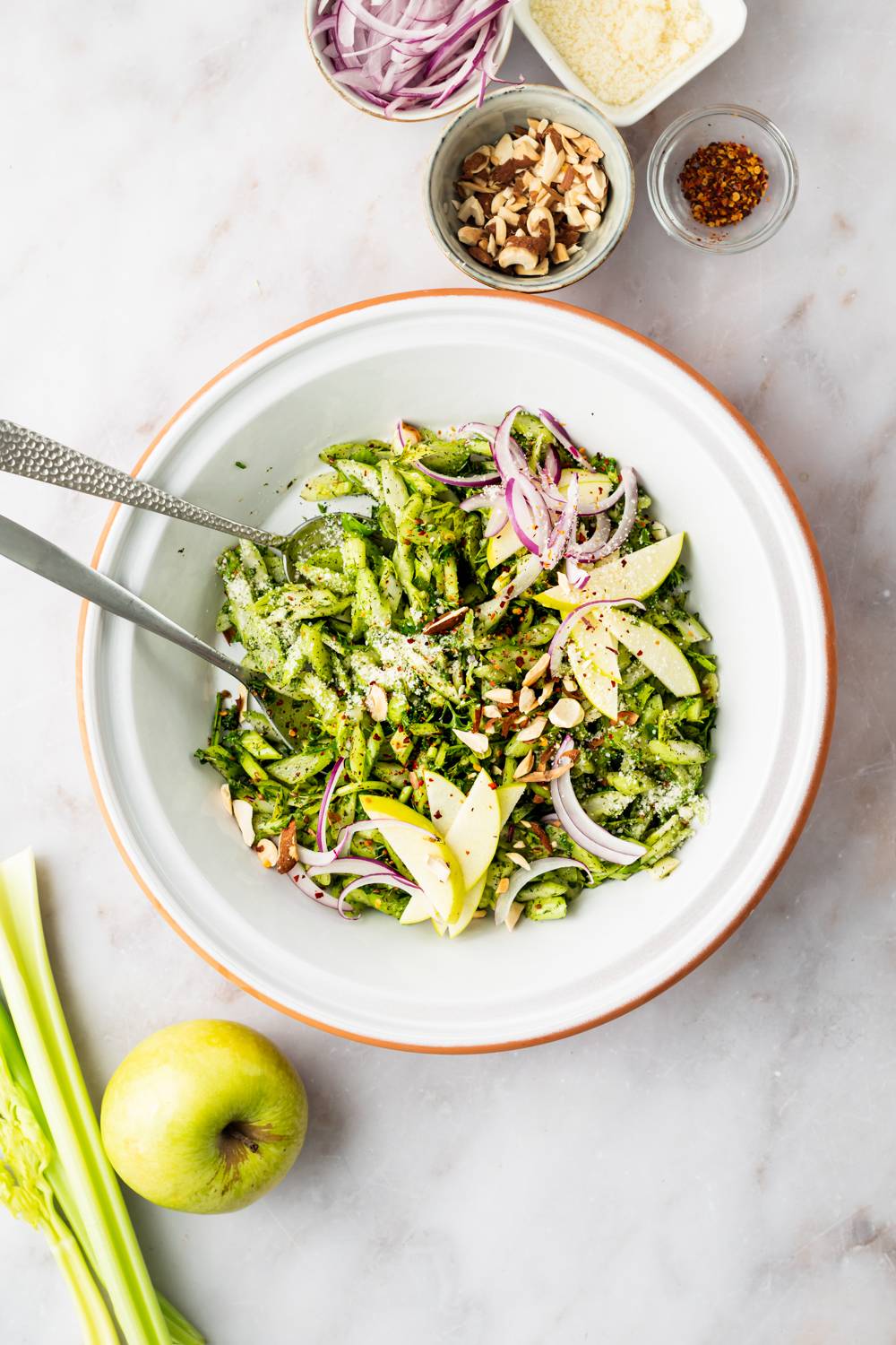 Celery and apple salad in a bowl with almonds, red onion, sliced red onion, and dressing.