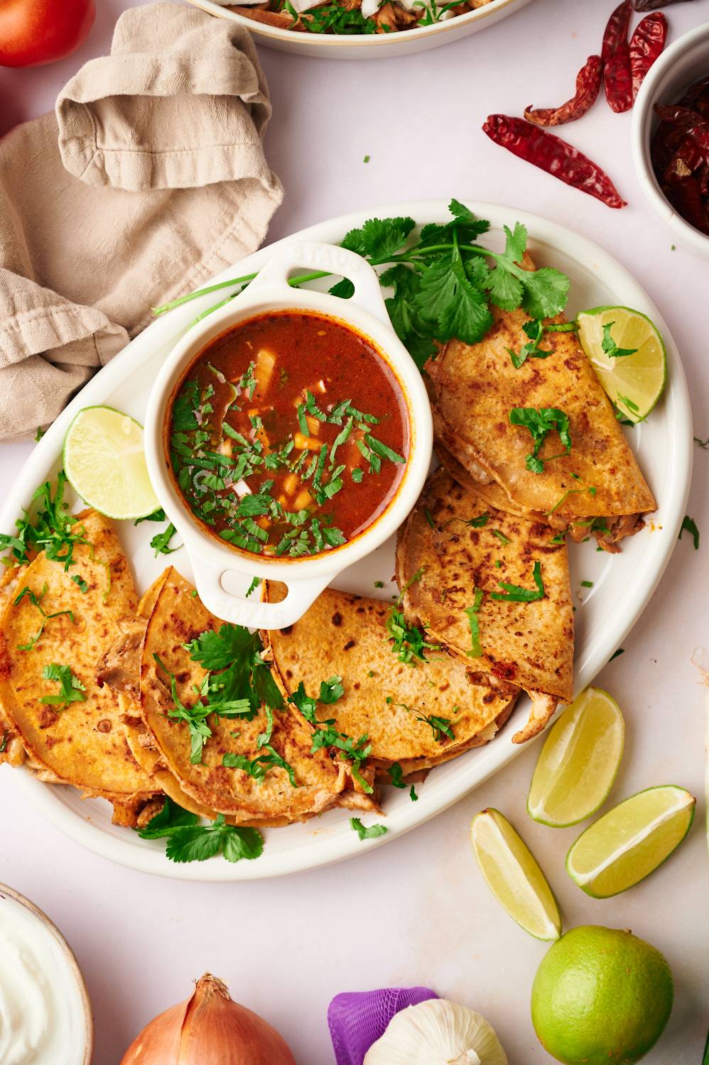 Chicken tacos cooked with birria sauce on a plate with dried chiles, limes, and onion on the side.