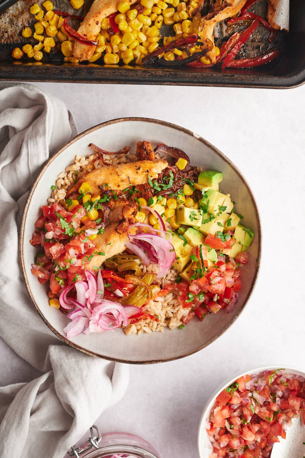 Easy chicken fajita bowls with chicken breast, bell peppers, onions, cron, salsa, and brown rice in a white bowl.