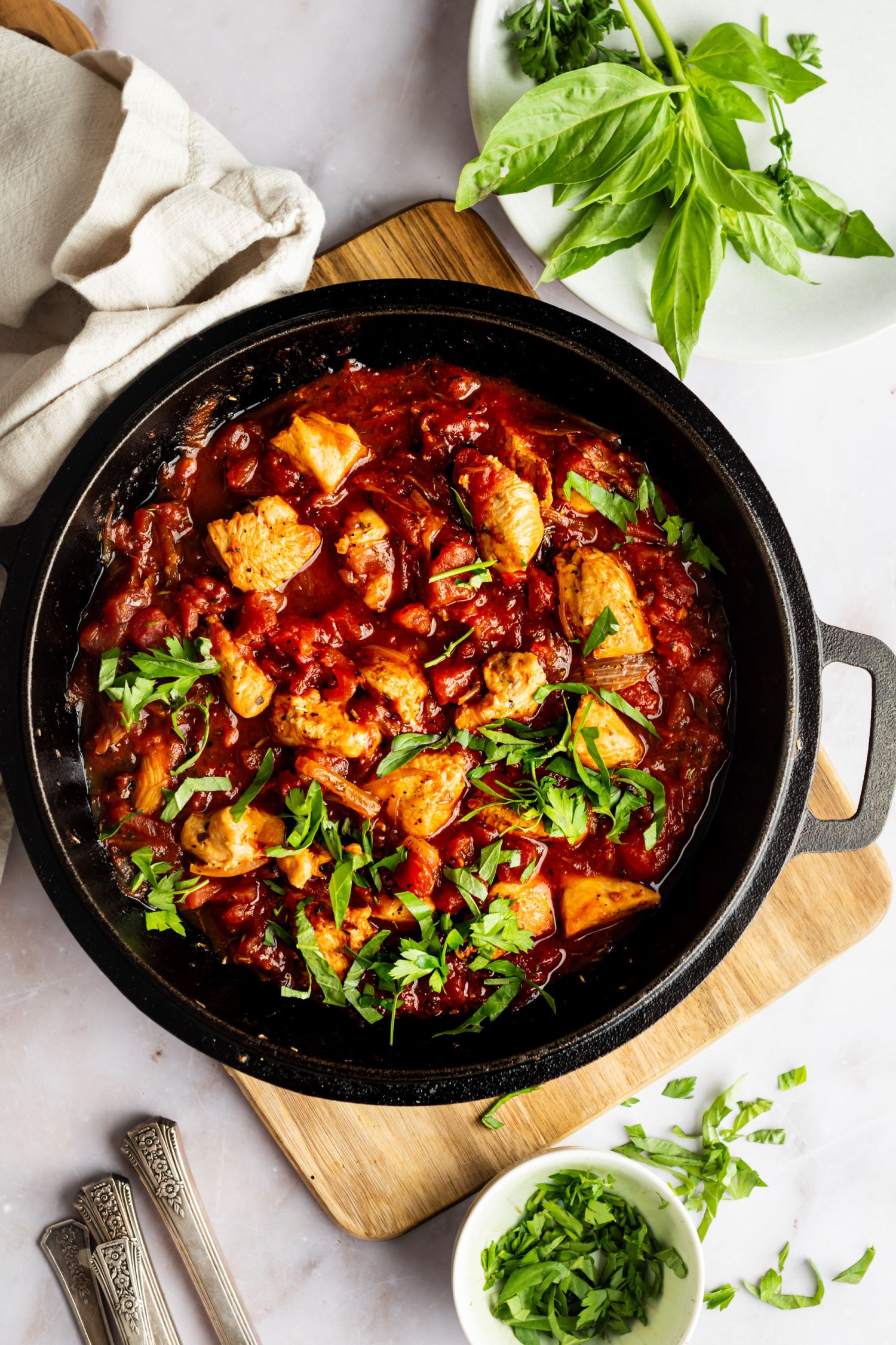 Fra Diavolo sauce with chicken in a skillet with fresh basil and parsley.