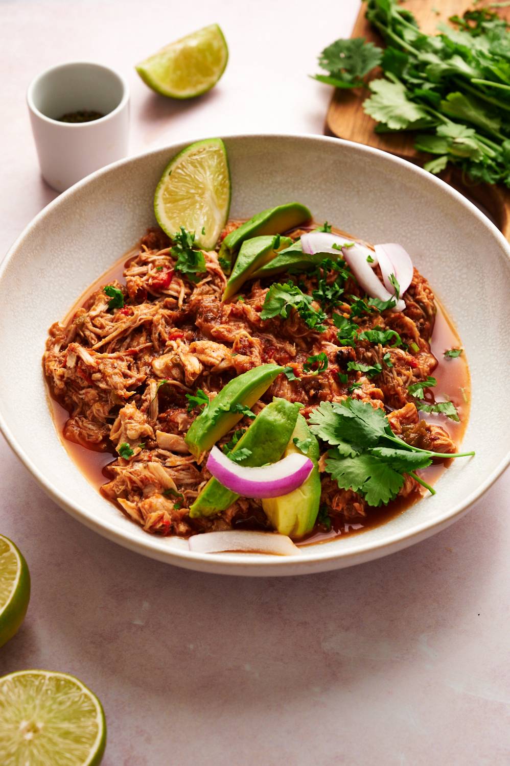 Homemade chicken machaca served with avocado, cilantro, red onion, and lime wedges.