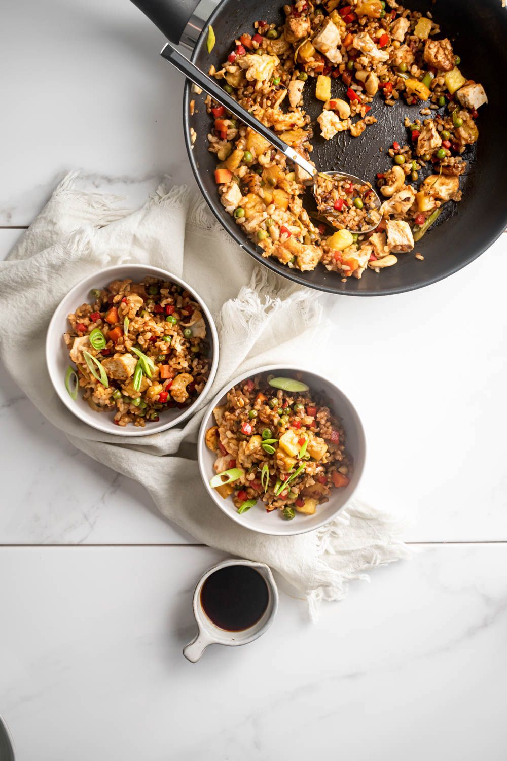 Brown fried rice with chicken, pineapple, veggies, and cashews in two bowls and a skillet.