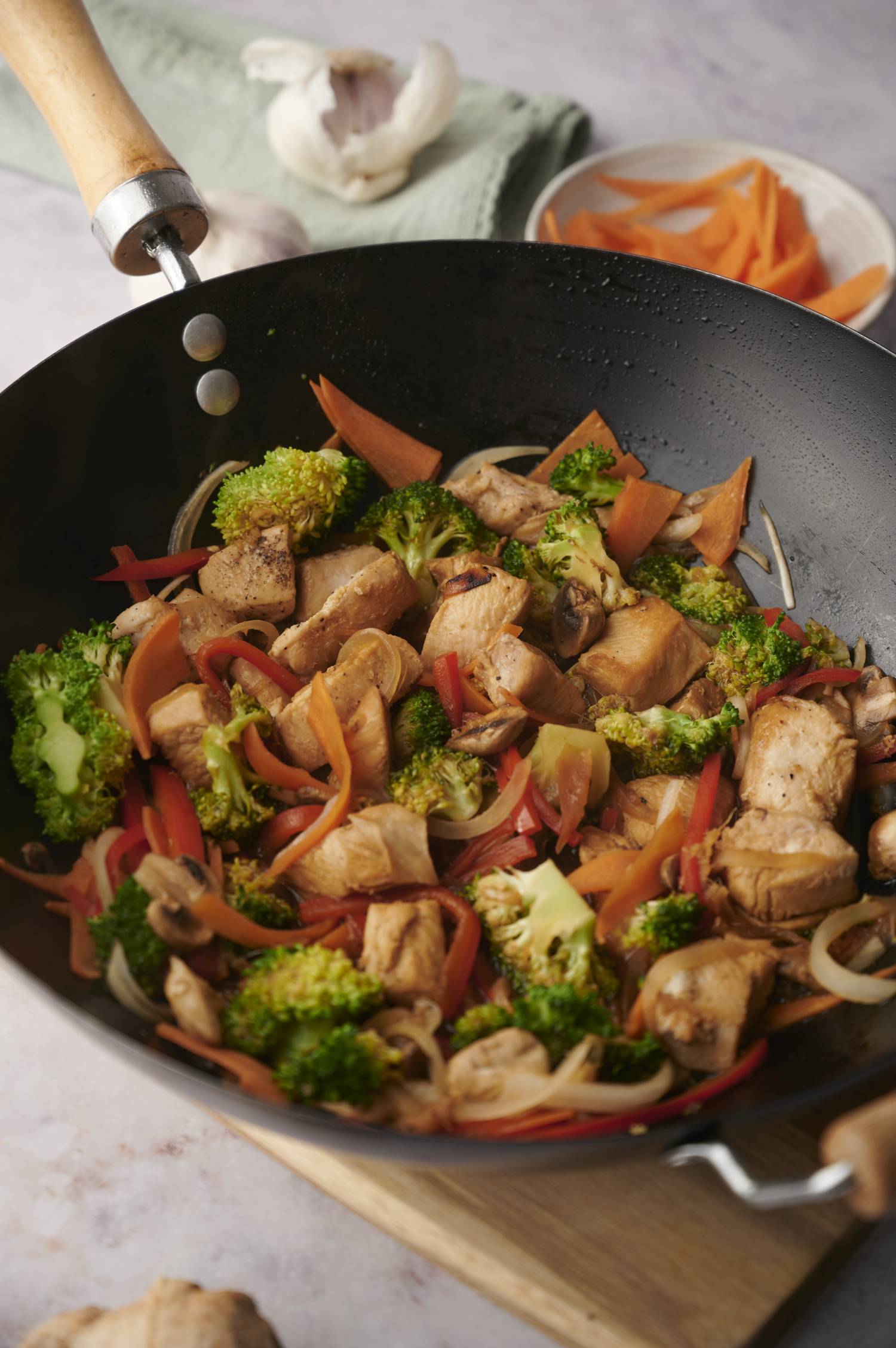 Stir fry chicken and vegetables in a wok with broccoli, chicken breast, peppers, carrots, and mushrooms.