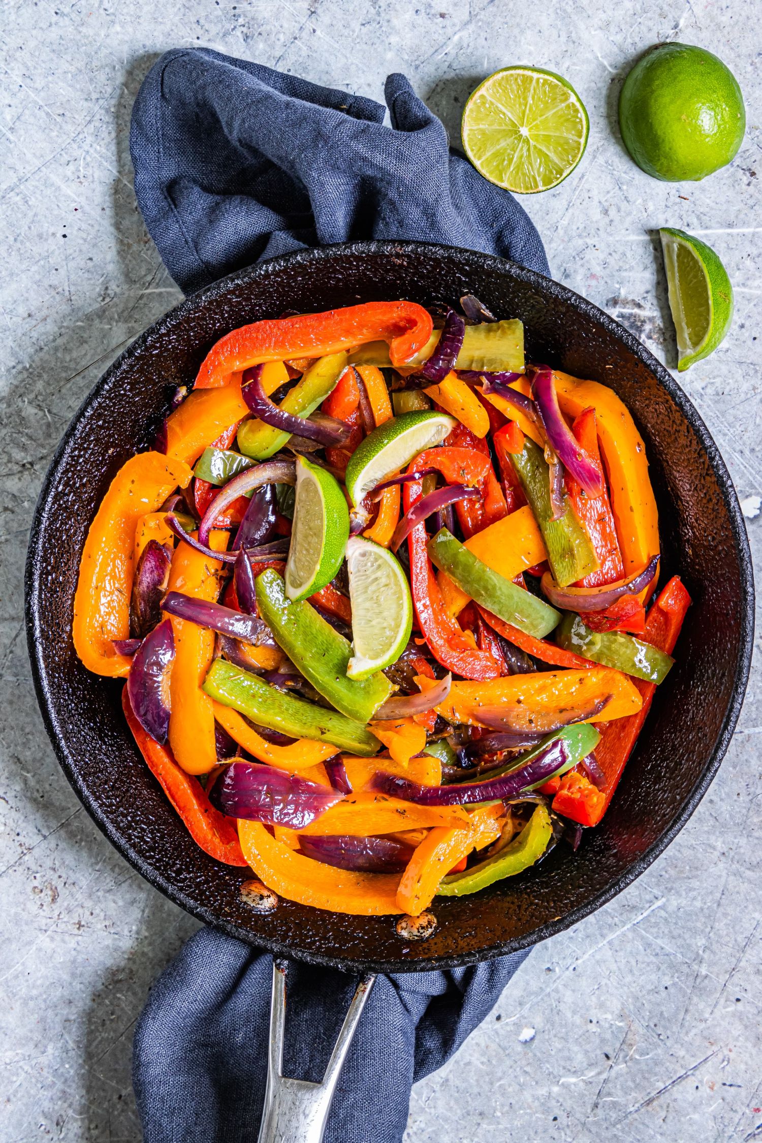 Skillet with fajita style bell peppers and onions served with fresh lime wedges.