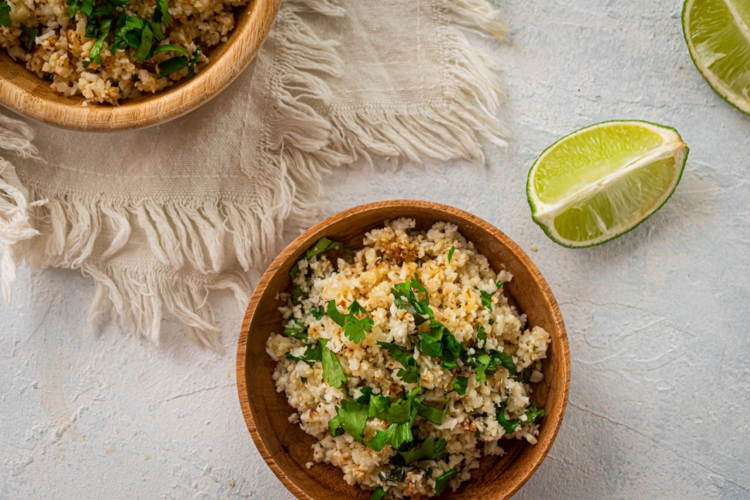 Cauliflower rice with cilantro leaves and fresh lime juice in a wooden bowl.