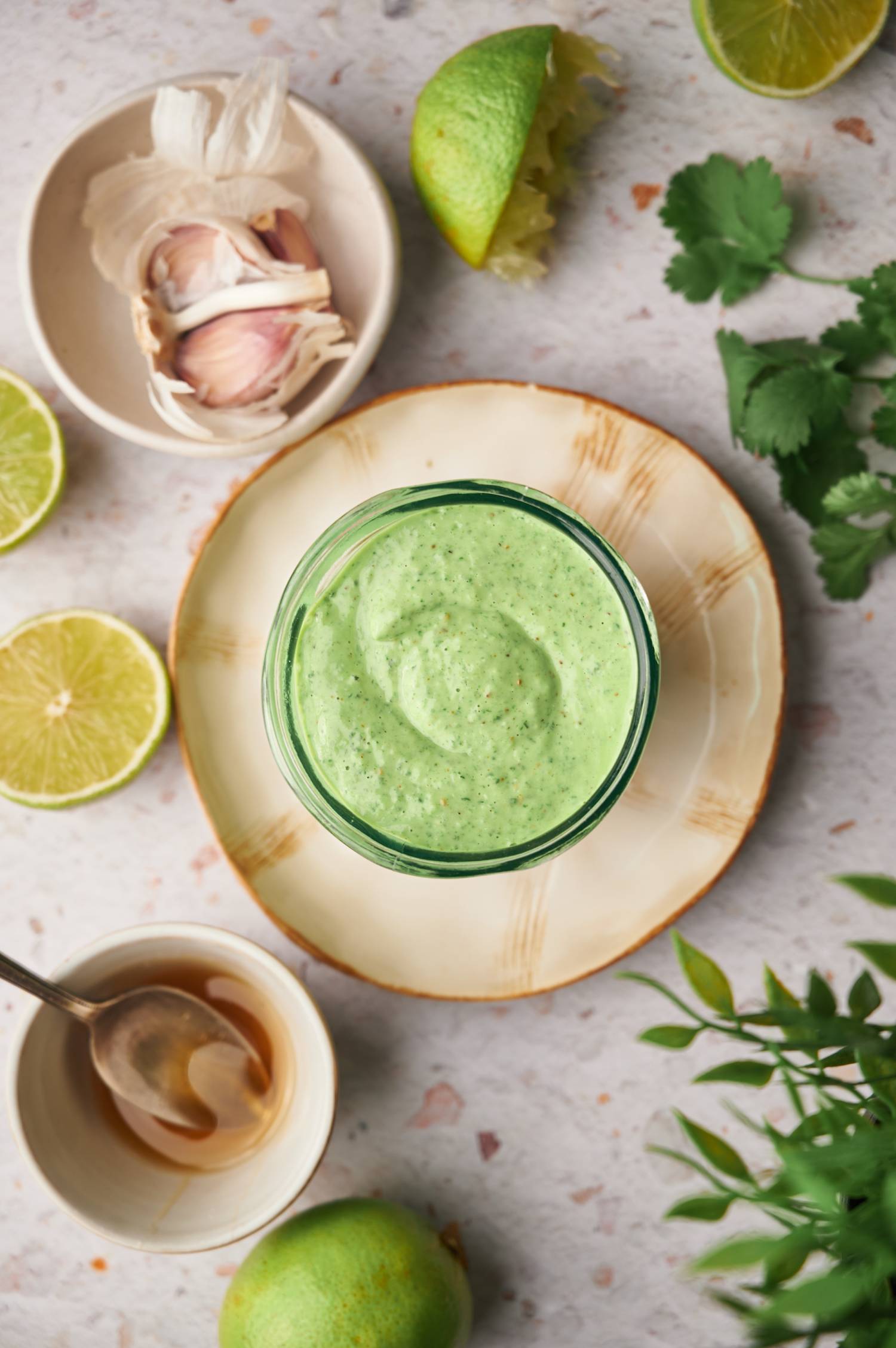 Cilantro lime yogurt sauce in a glass jar with garlic, cilantro, honey, and lime wedges on the side.