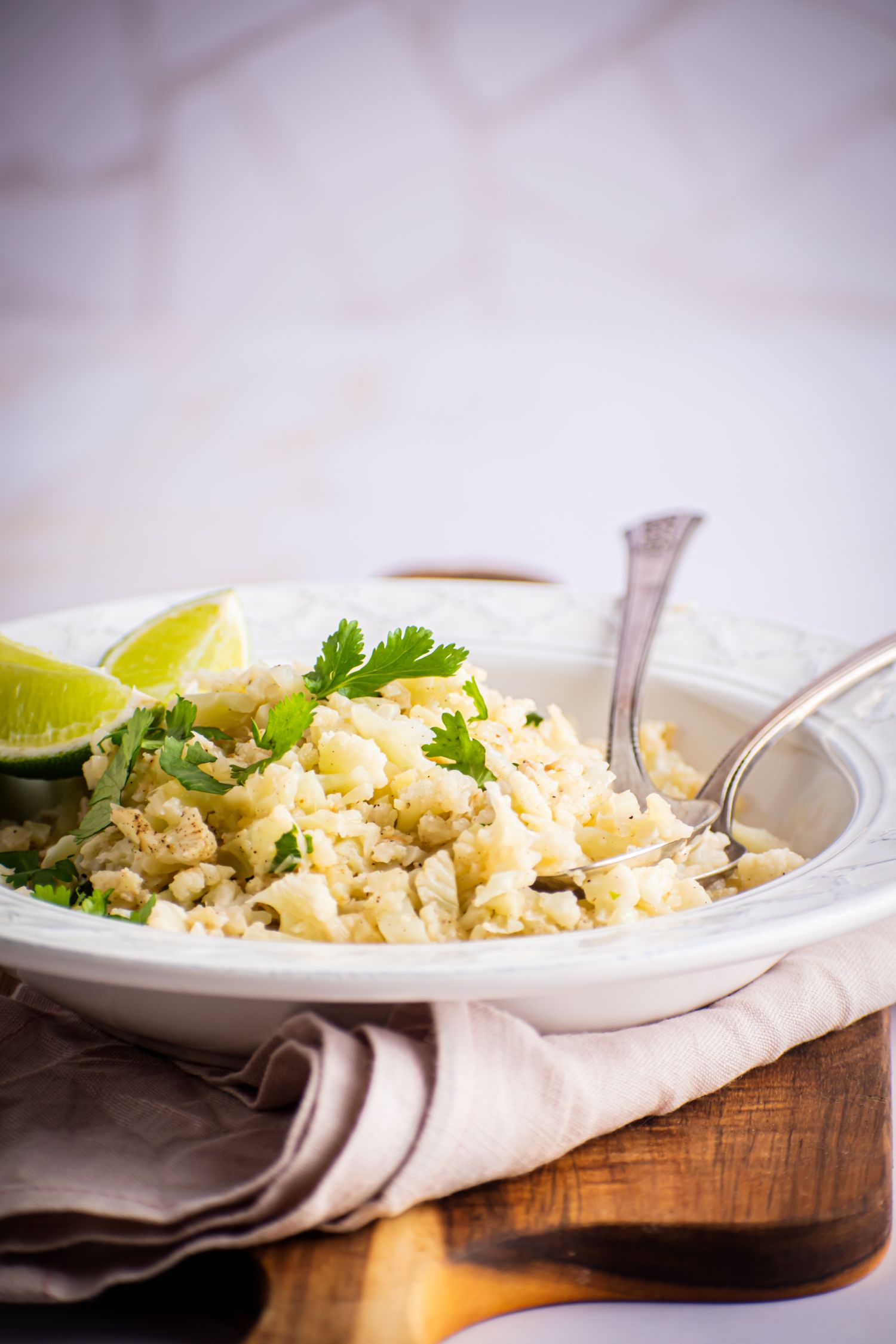 Bowl of coconut cauliflower rice with garlic, ginger, coconut milk, cilantro, and lime wedges. 