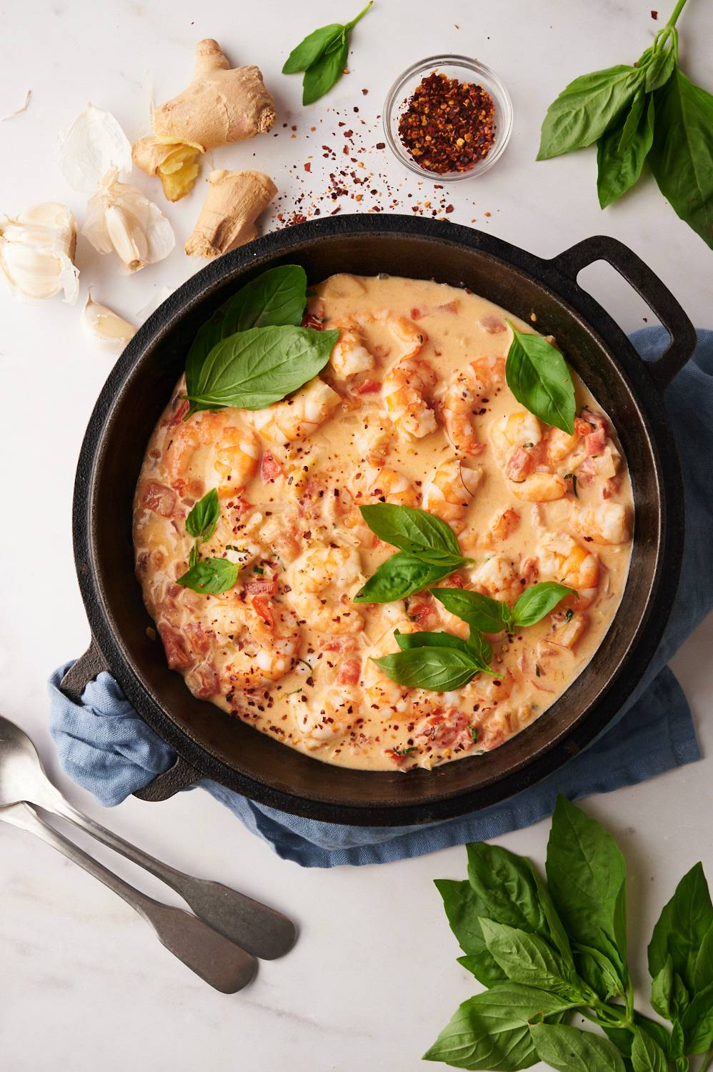 Creamy coconut and tomato shrimp in a skillet with fresh basil leaves.