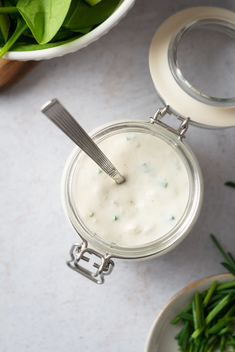 Homemade gorgonzola salad dressing in a glass jar with salad greens and chives on the side.