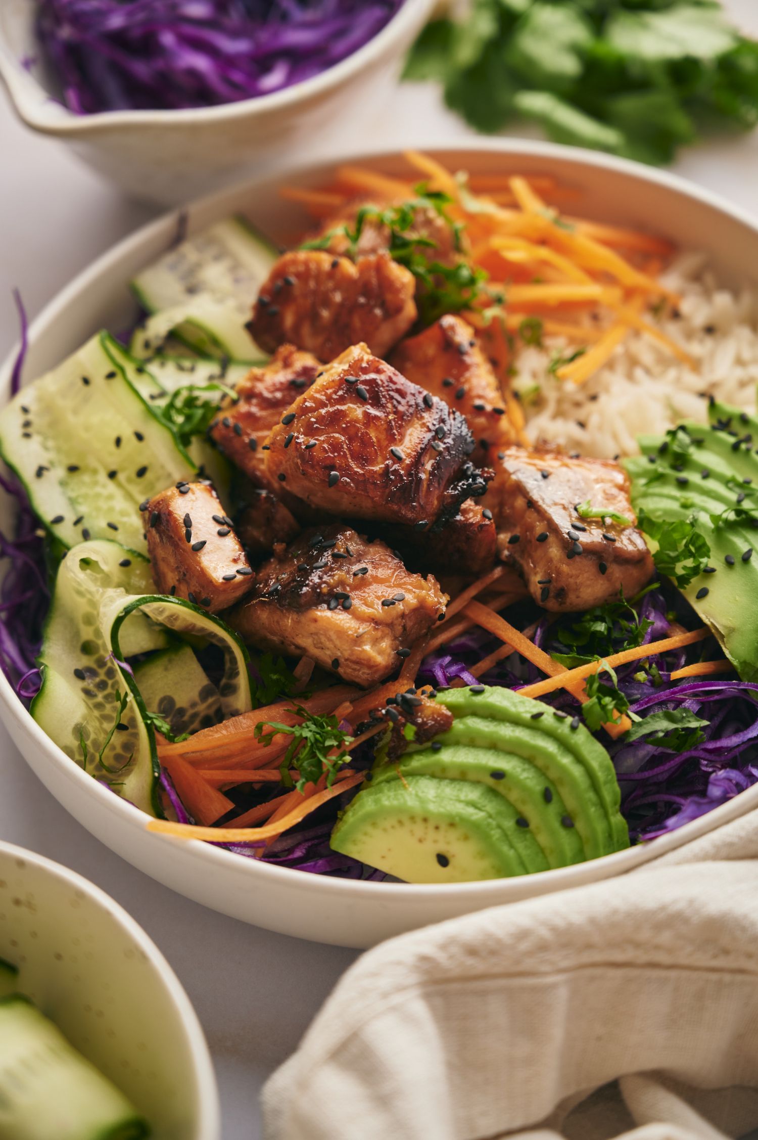 Asian salmon and rice bowl with avocado, carrots, cabbage, sesame seeds, carrots, and white rice. 