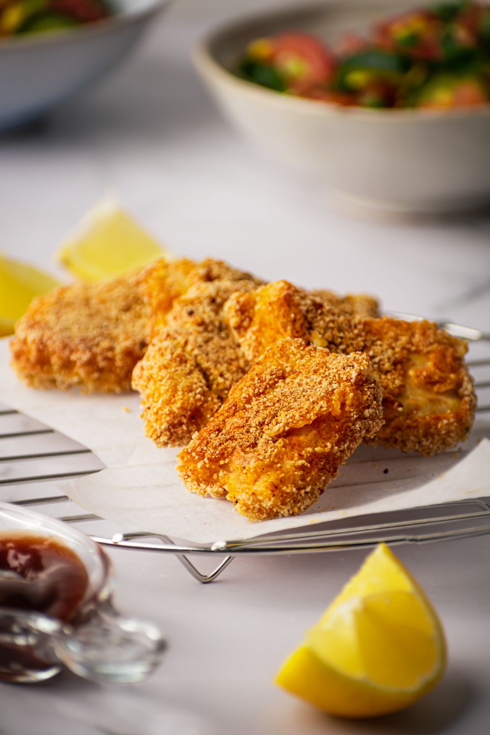 Crispy oven baked fish with a seasoned coating served on parchment paper with lemon and salad.