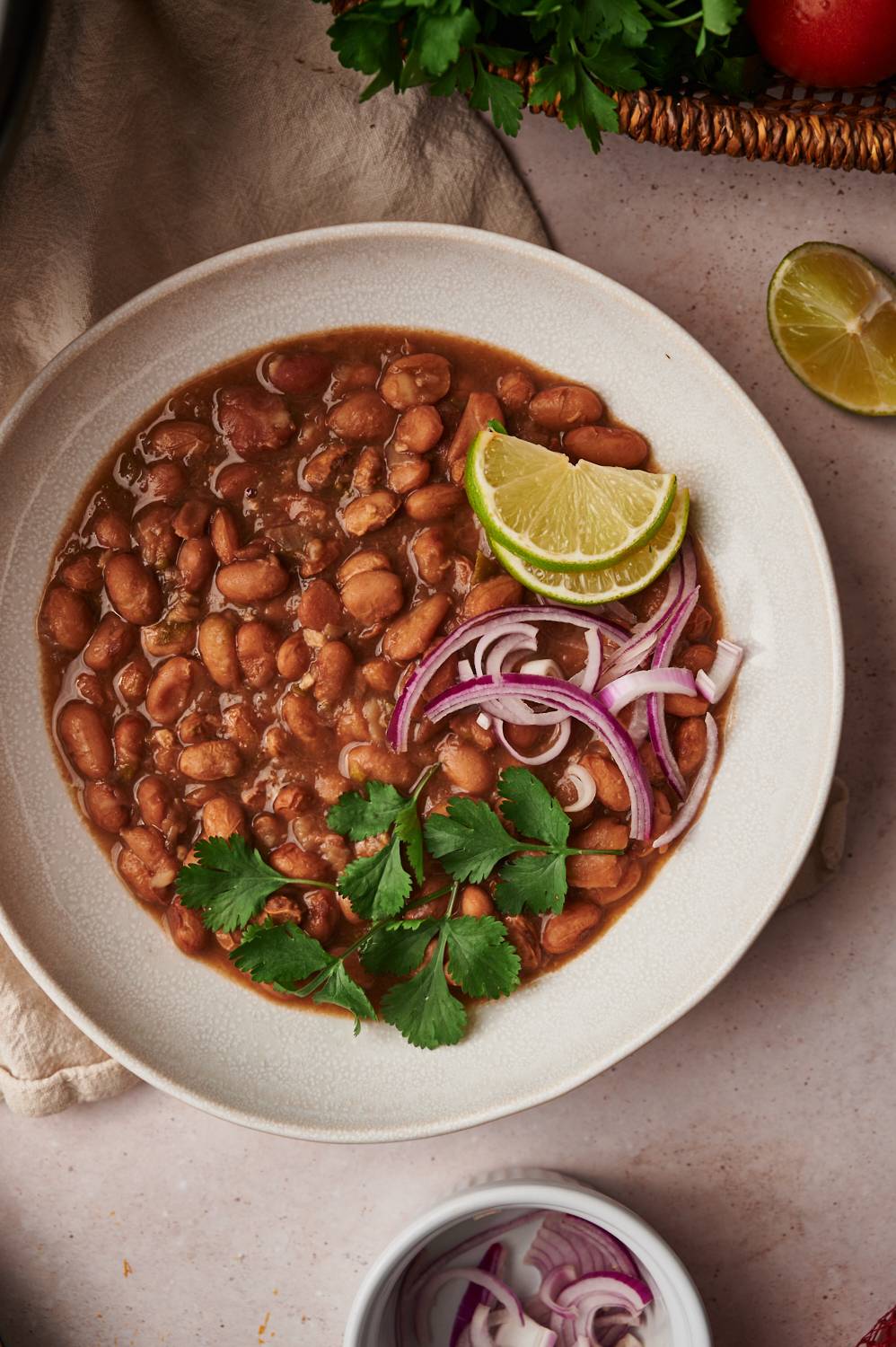 Bowl of slow cooked pinto beans in a bowl with cilantro, onion, tomato, and lime.