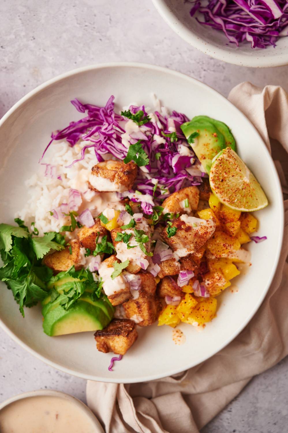 Taco bowls with seasoned fish, avocado, mango salsa, white rice, and shredded red cabbage.