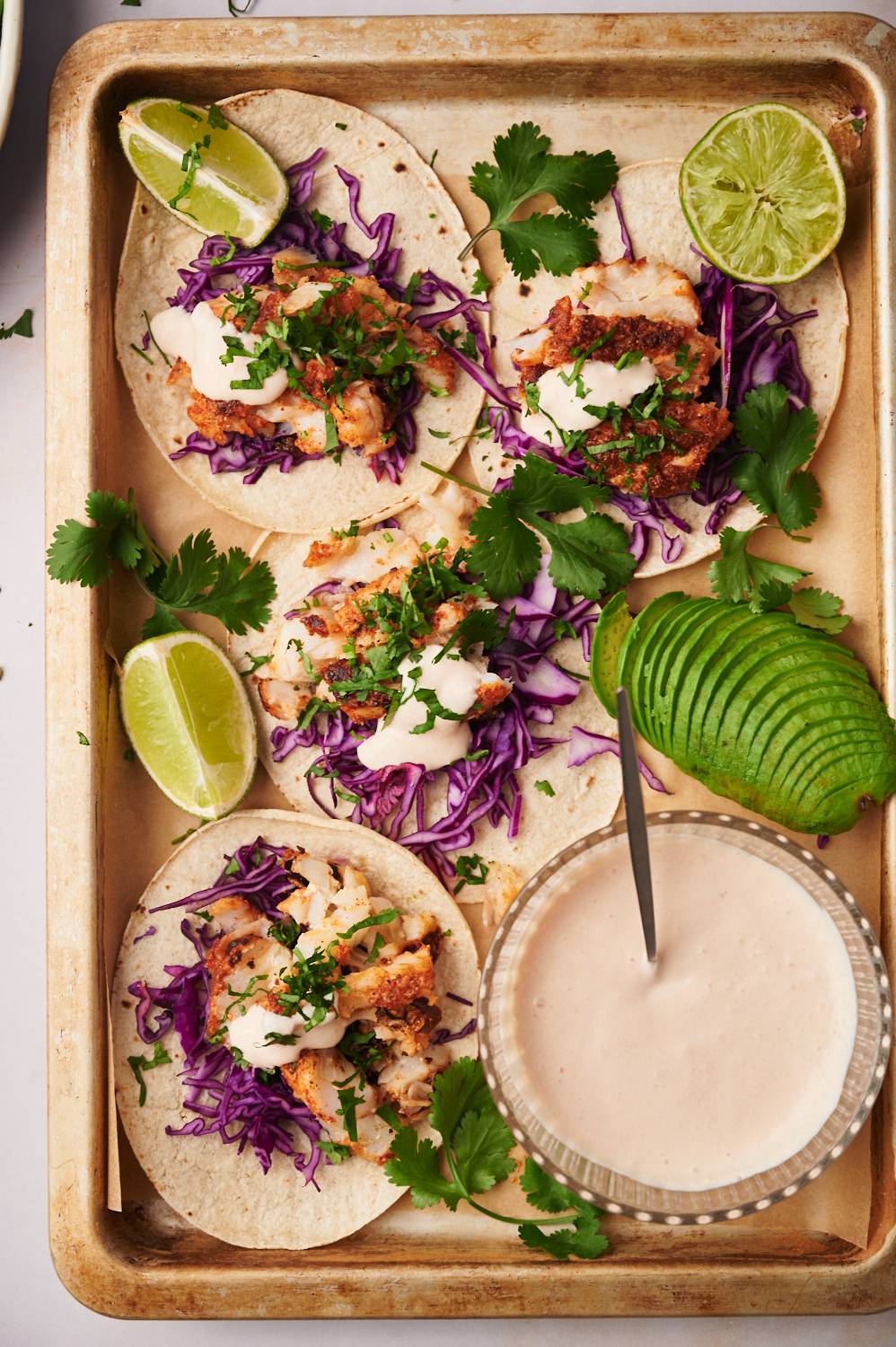 Creamy fish taco sauce in a bowl with fish tacos on the side served with cilantro and limes.