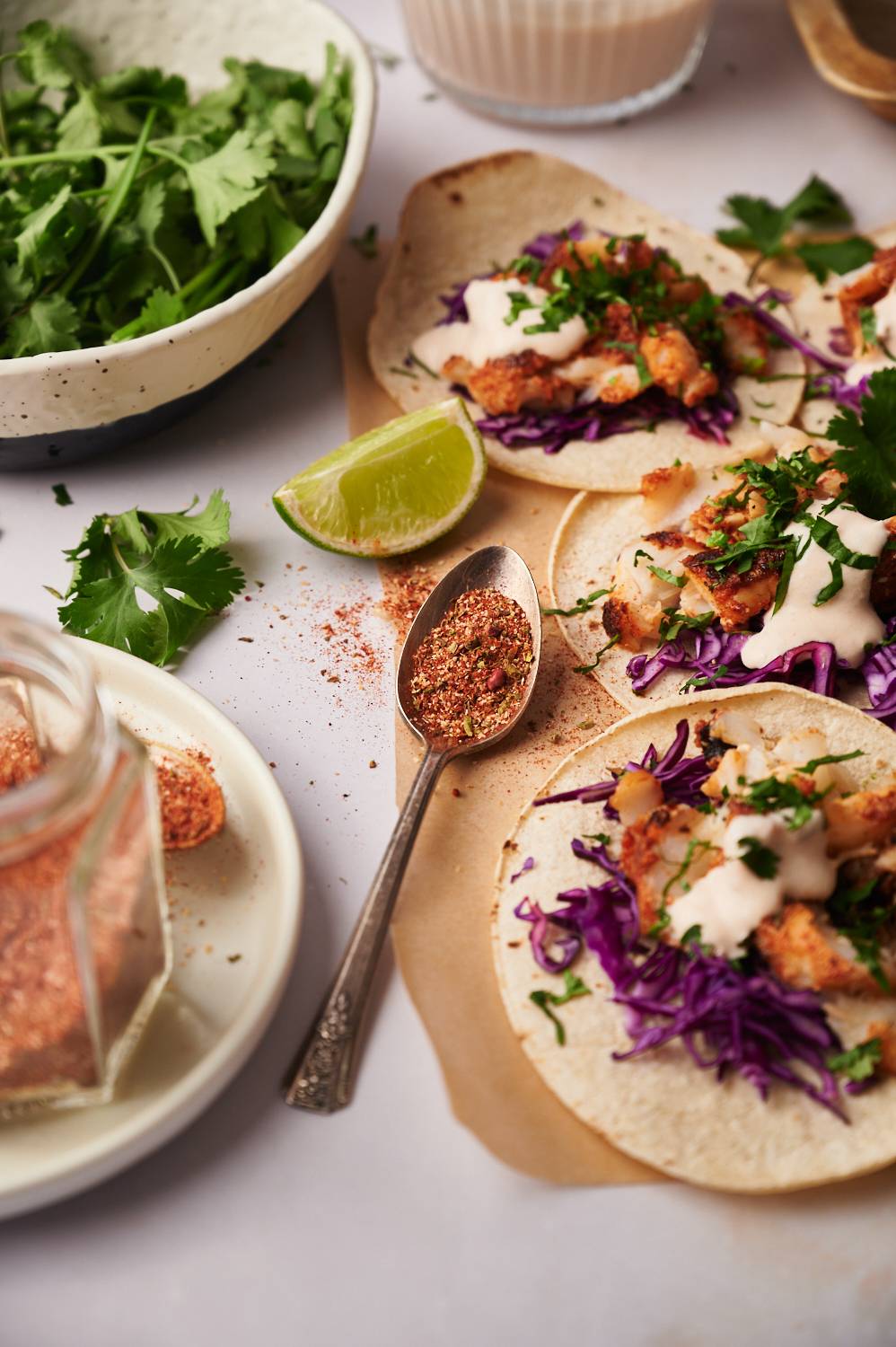 Homemade fish taco seasoning in a jar and served with fish tacos, limes, and cilantro.