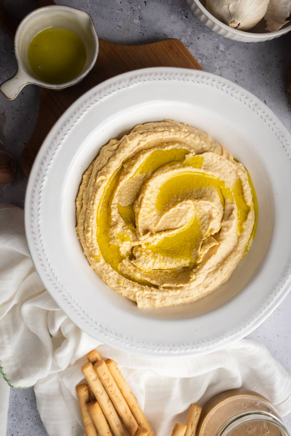 Bowl of garlic hummus with olive oil, chickpeas, tahini, and roasted garlic served with oil and breadsticks.