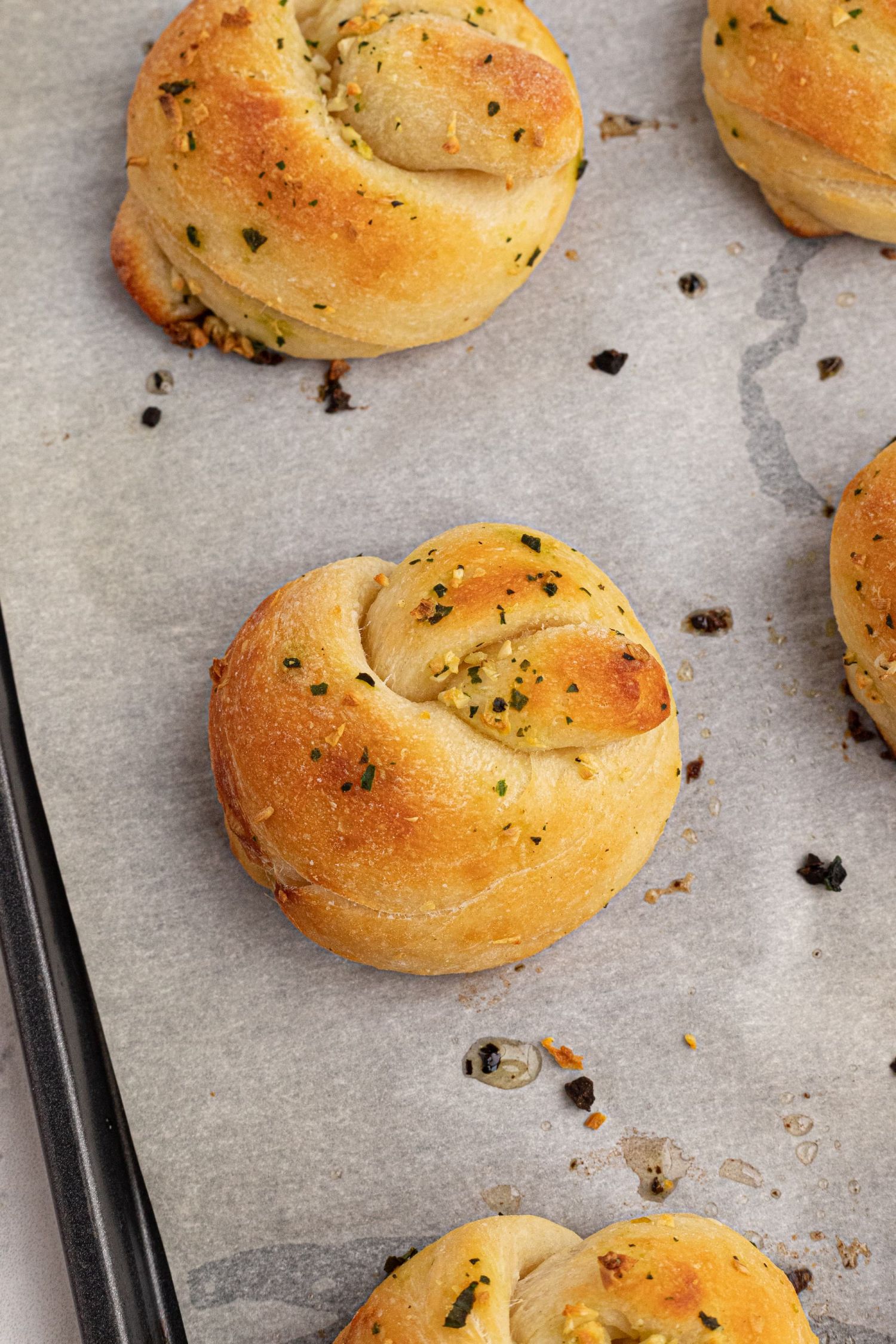 Baked garlic knots with fresh garlic, basil, and butter on a baking sheet with parchment paper.