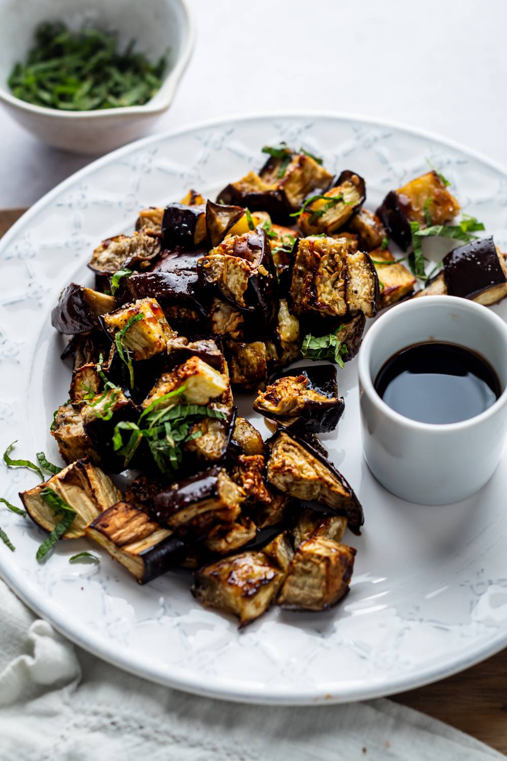 Roasted garlic eggplant served on a plate with balsamic vinegar and fresh basil.