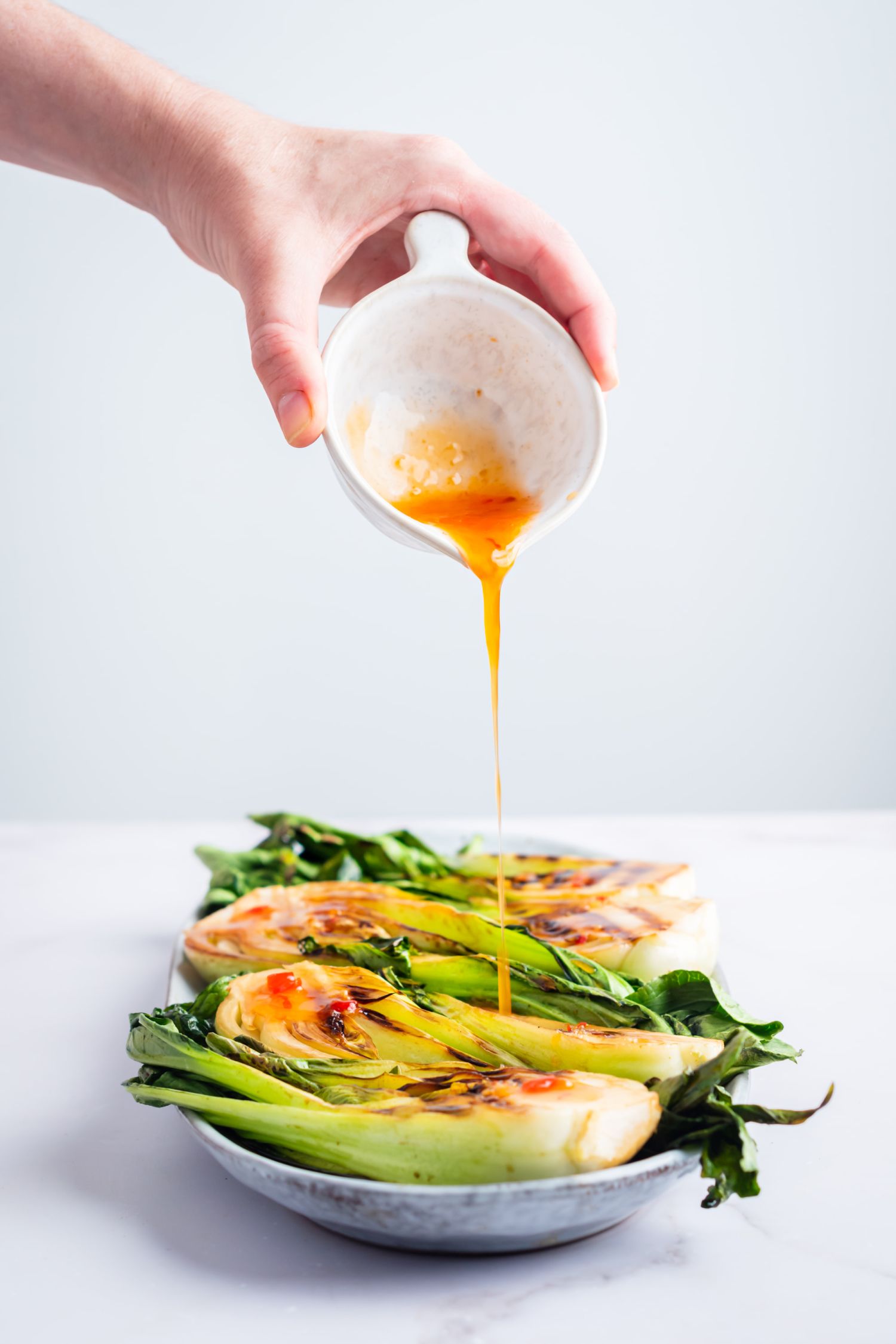 Bok choy with grill marks on a plate with someone pouring Asian sauce on top. 