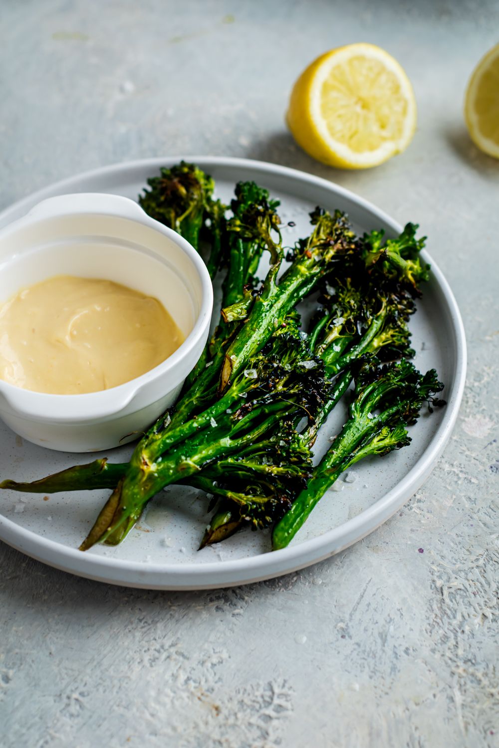 Easy grilled broccolini served on a white plate with dipping sauce and fresh lemon juice.