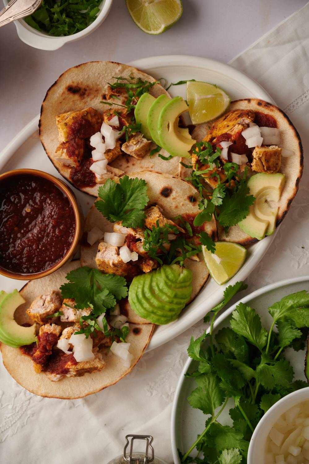 Tacos with grilled chicken, avocado, cilantro, onions, and red salsa on corn tortillas.