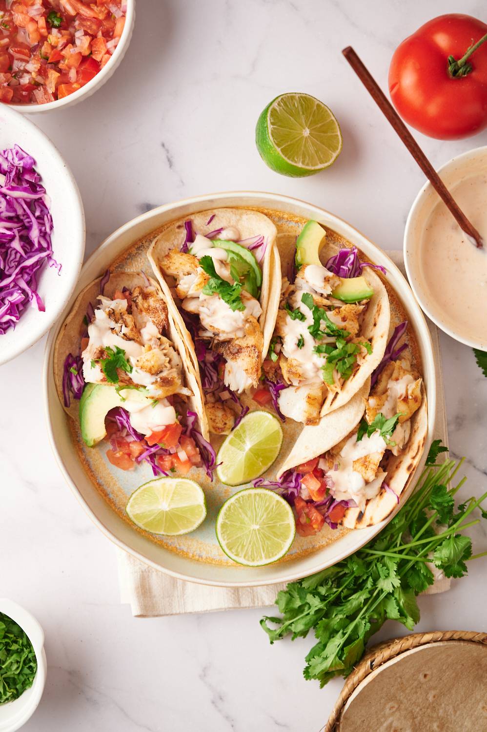 Plate of grilled fish tacos with red cabbage, grilled white fish, lime, avocado, and salsa.