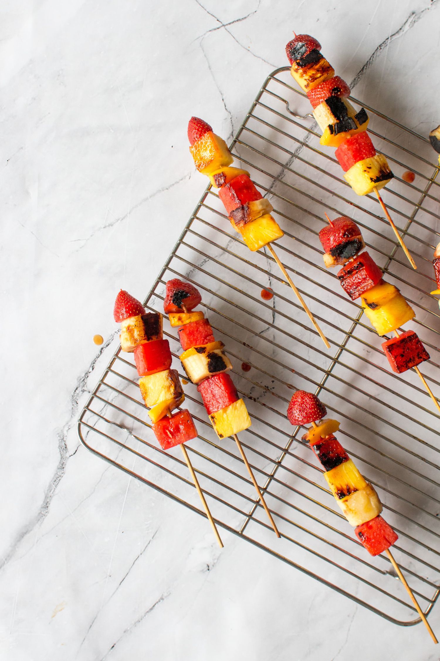 Kabobs with grilled fruit including bananas, watermelon, mango, and pineapple on a wire rack.