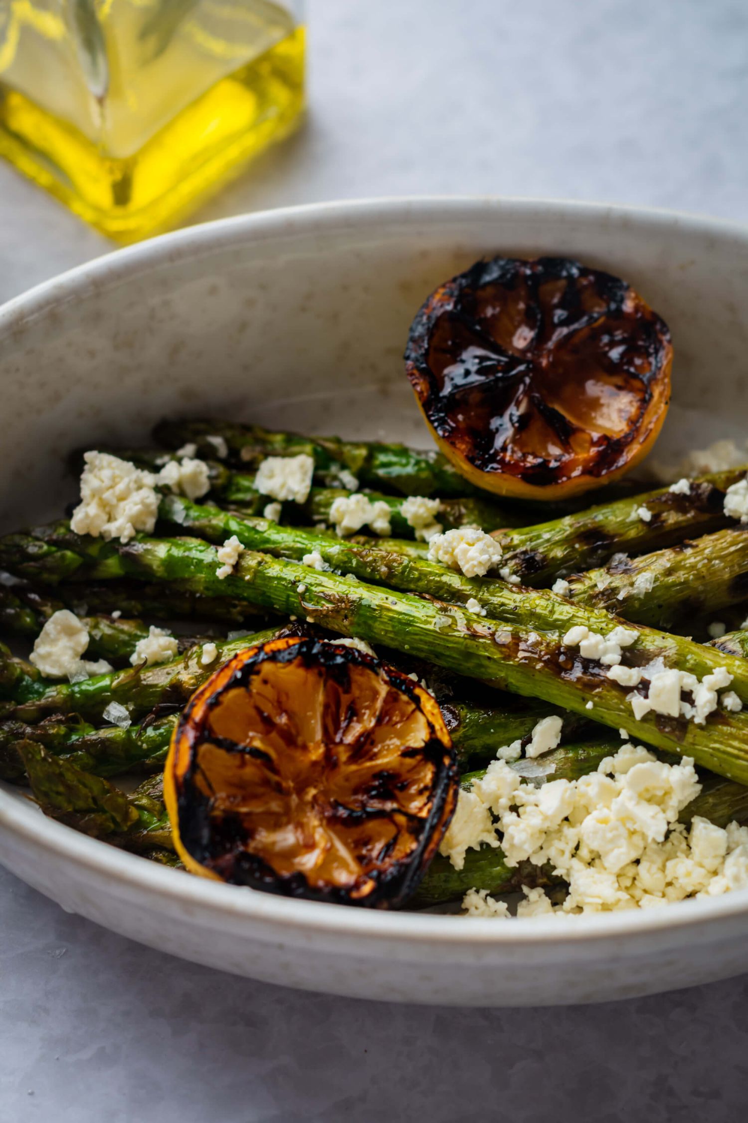 Bowl of grilled asparagus served with lemon juice, black pepper, and feta cheese.