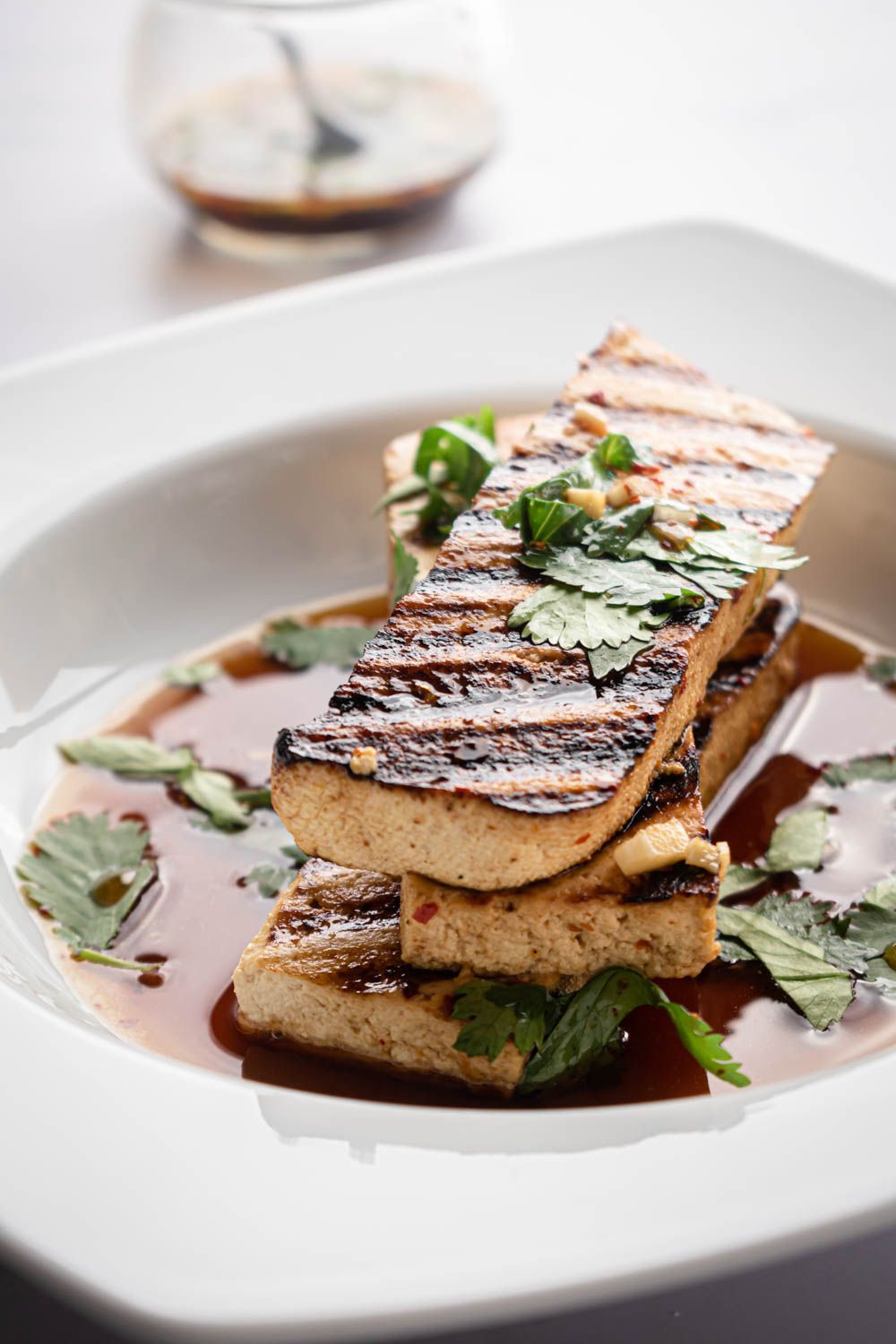 Bowl of grilled tofu slices with an Asian sauce drizzled on top and fresh cilantro leaves.