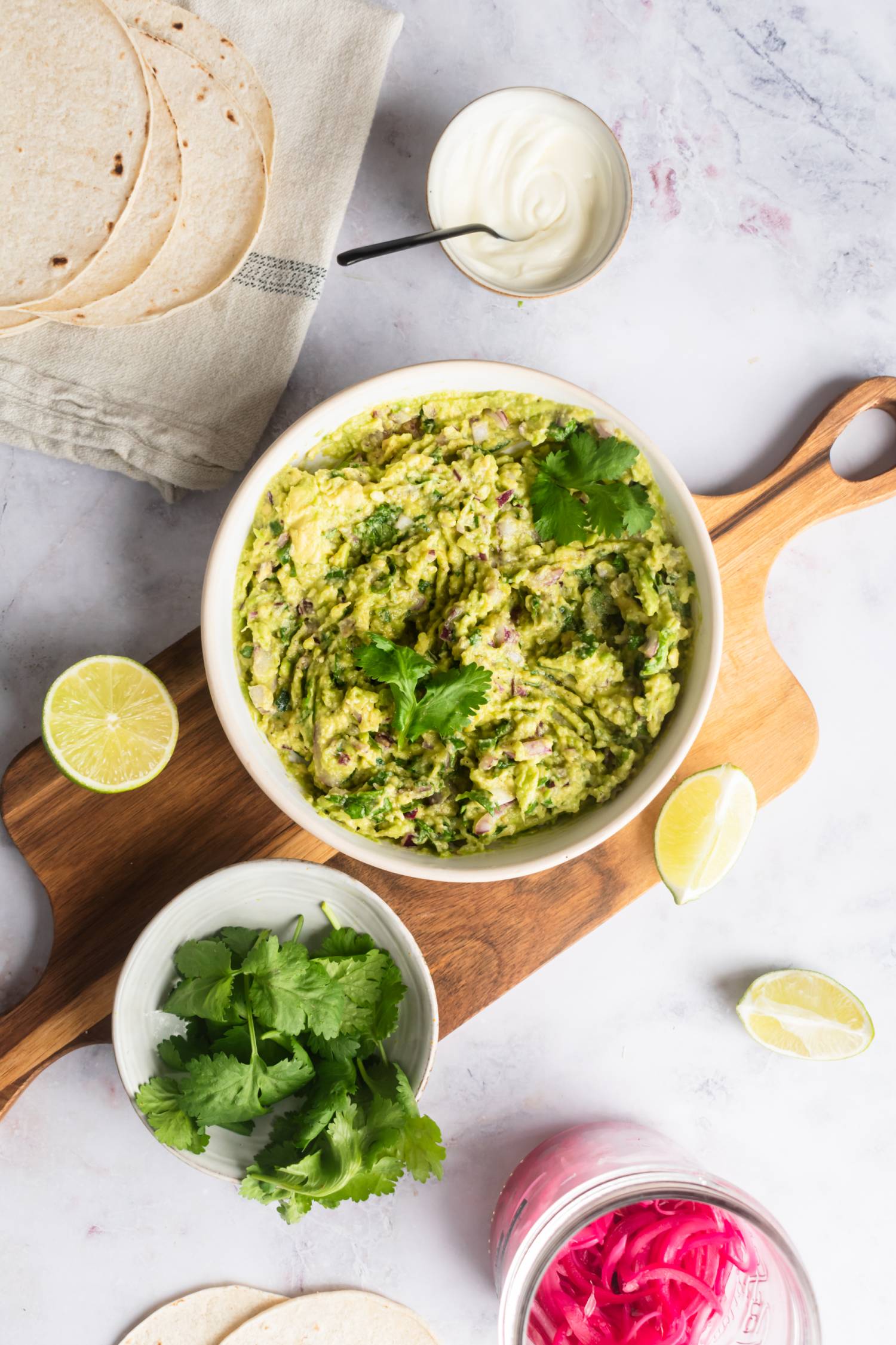 Mexican guacamole with cilantro, lime juice, mashed avocados, and onion in a bowl with tortillas on the side.