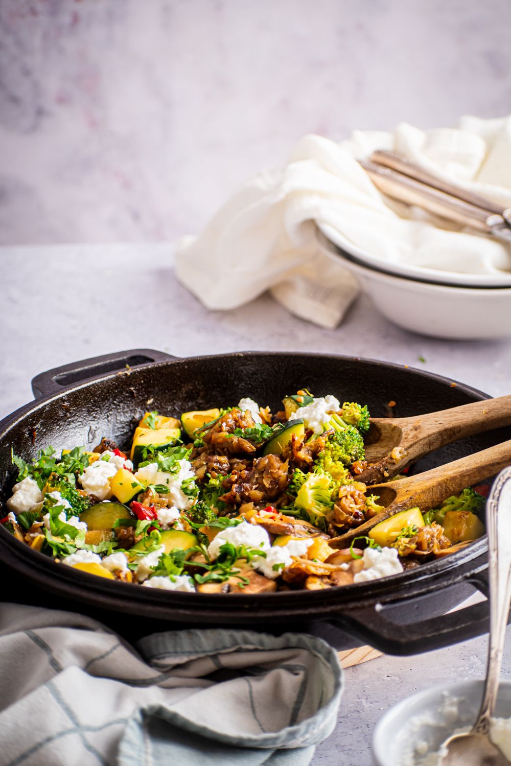 Cast iron skillet filled vegetable and potato hash and topped with feta cheese and herbs.