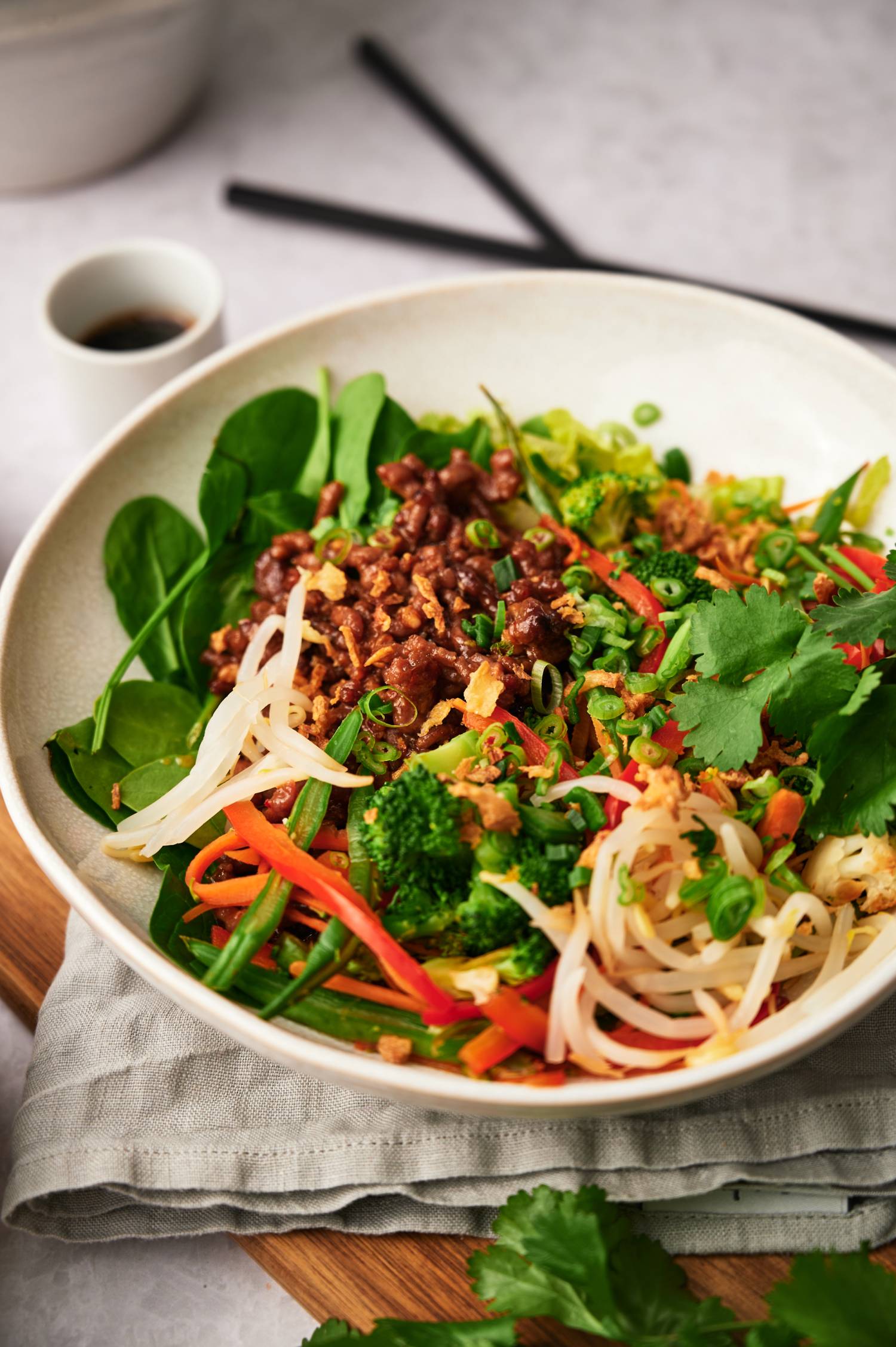 Korean ground beef bowls with green onions, carrots, spinach, bell peppers, green beans, and cilantro in a white bowl.