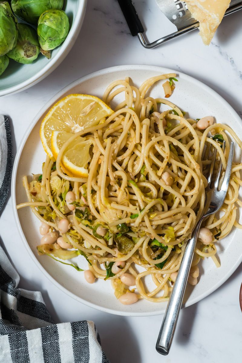 Pasta with shredded Brussels sprouts, lemon, white beans, and parmesan cheese on a white plate.