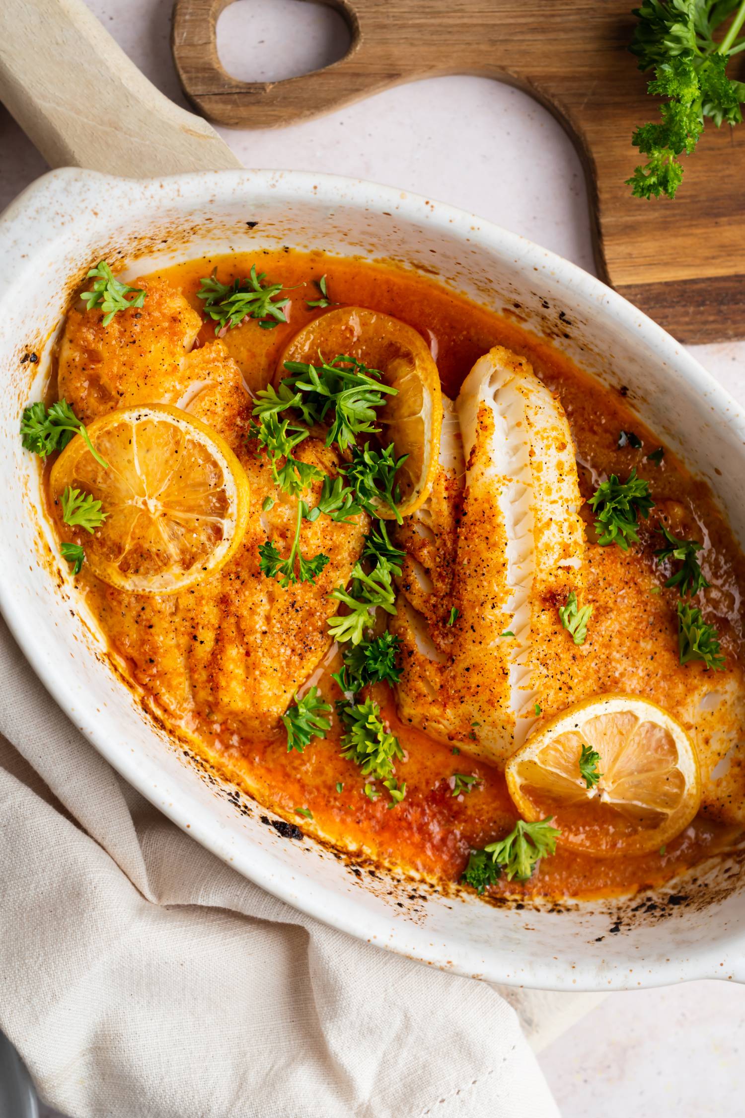 Baked lemon pepper tilapia with fresh lemon slices, butter, parsley, and lemon pepper seasoning in a baking dish.