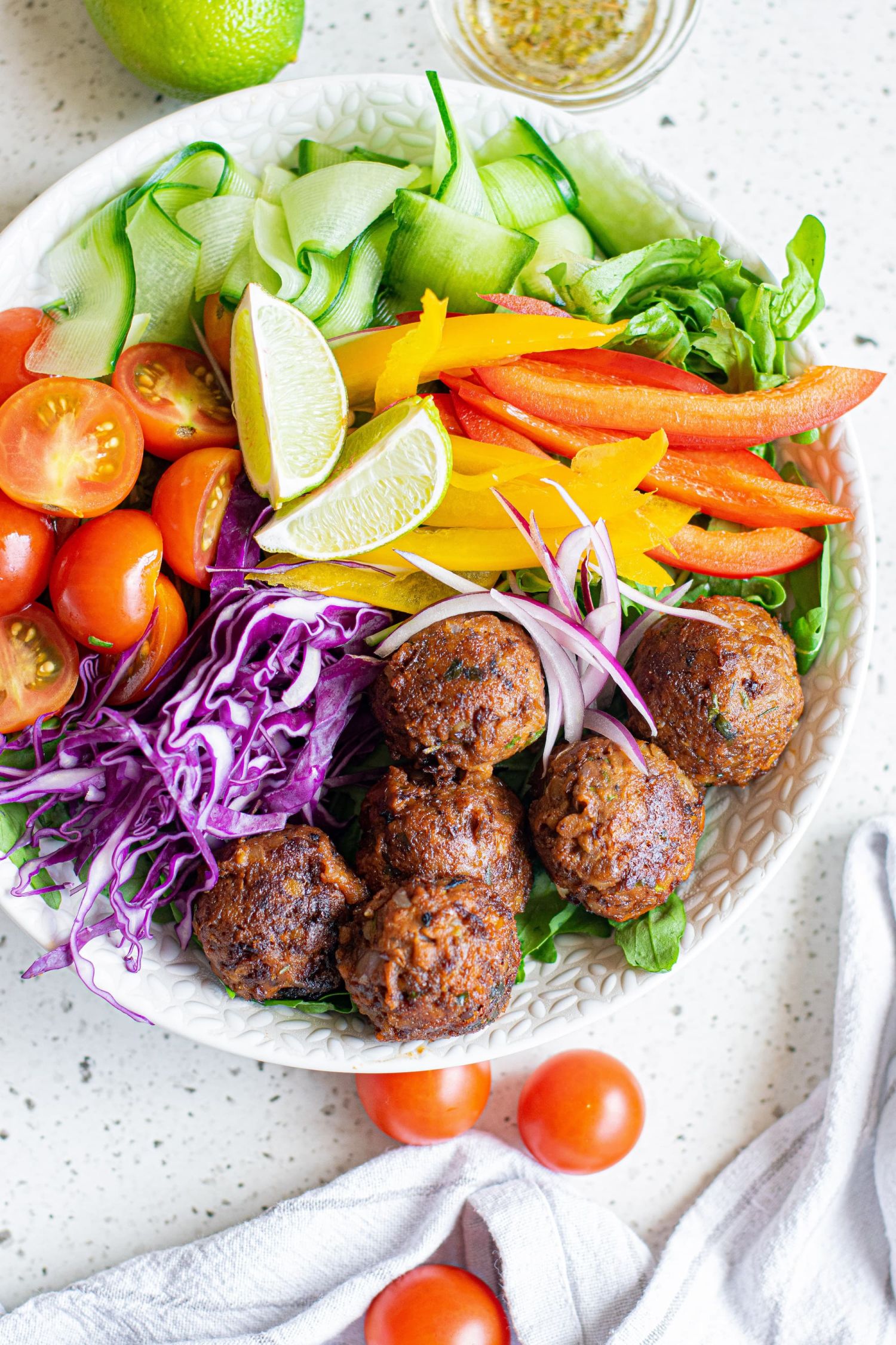 Plant based lentil balls with crispy edges served with fresh veggies in a bowl.