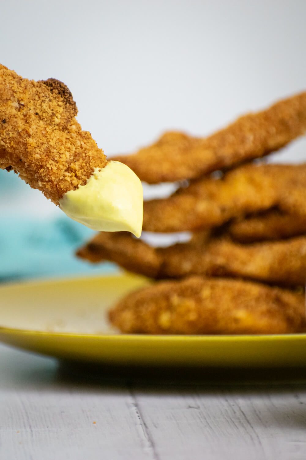 Almond crusted chicken tenders  being dipped in honey mustard with chicken tenders on a plate.