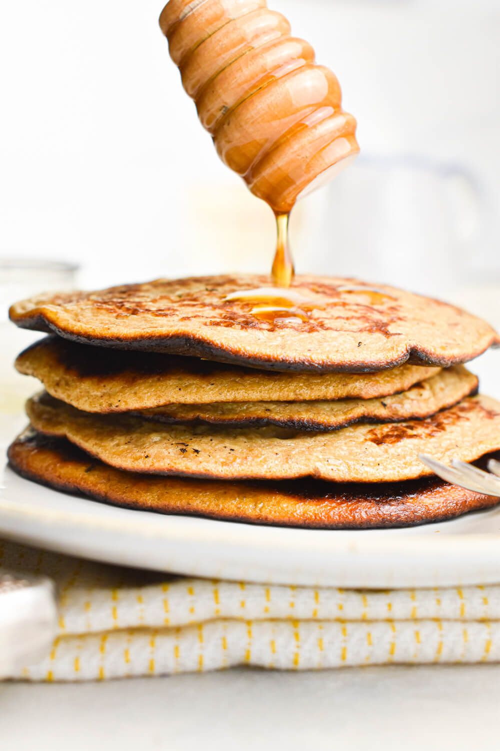 Banana Flaxseed Pancakes stacked on a plate with syrup being drizzled on top.